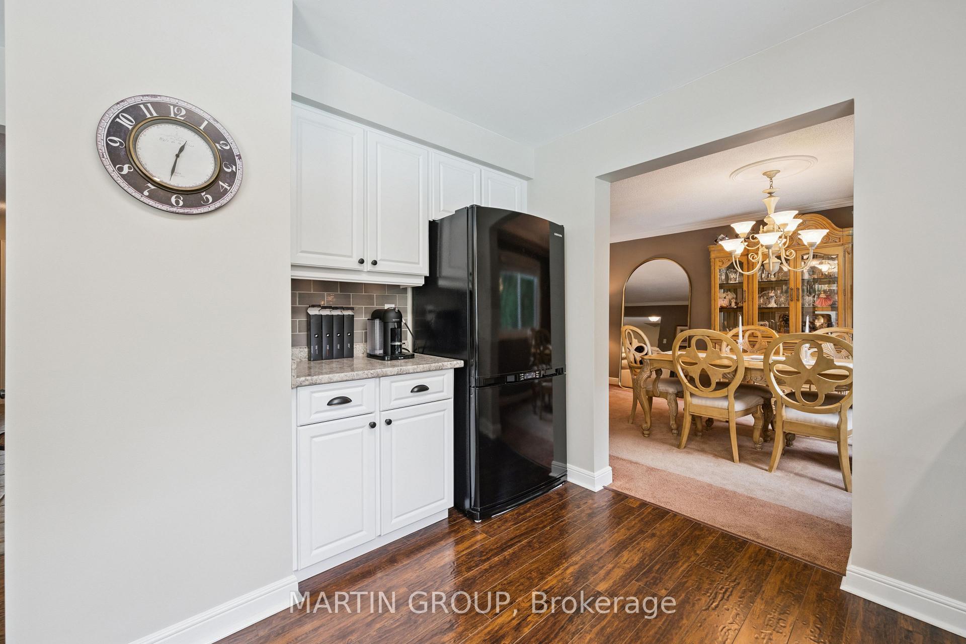 Kitchen with white cabinets and black refrigerator opening to a dining room with a wooden table.