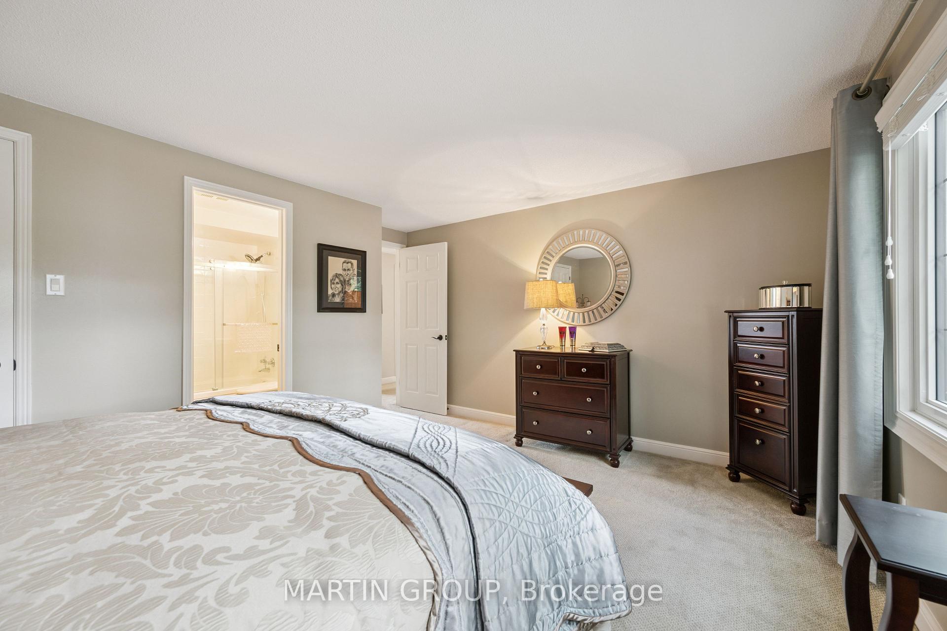 Furnished bedroom with patterned bedding, dark dressers, and an open doorway to a bright bathroom.
