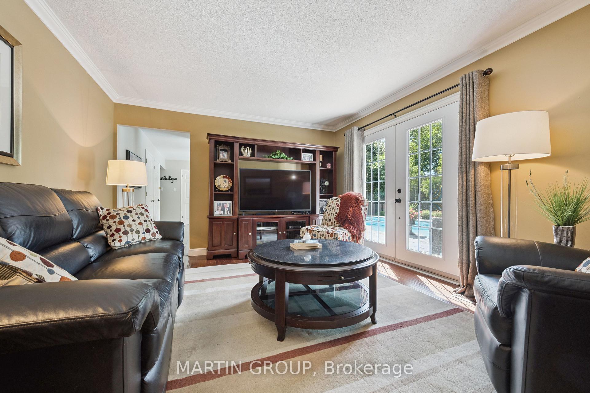 Furnished living room with leather sofas, a round coffee table and French doors overlooking a pool.