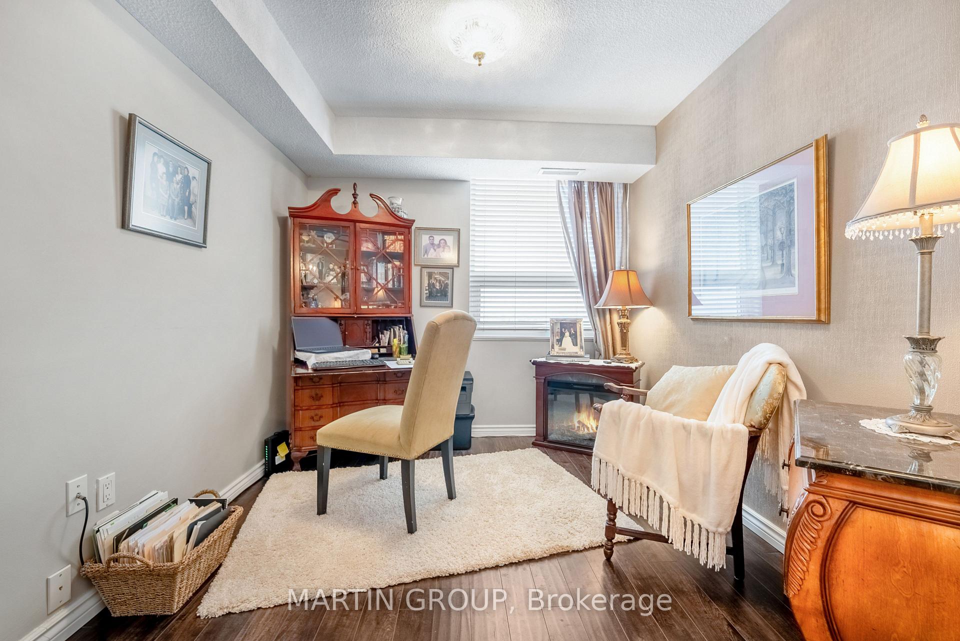 Furnished den with a wooden desk, small fireplace, armchair, and large window.