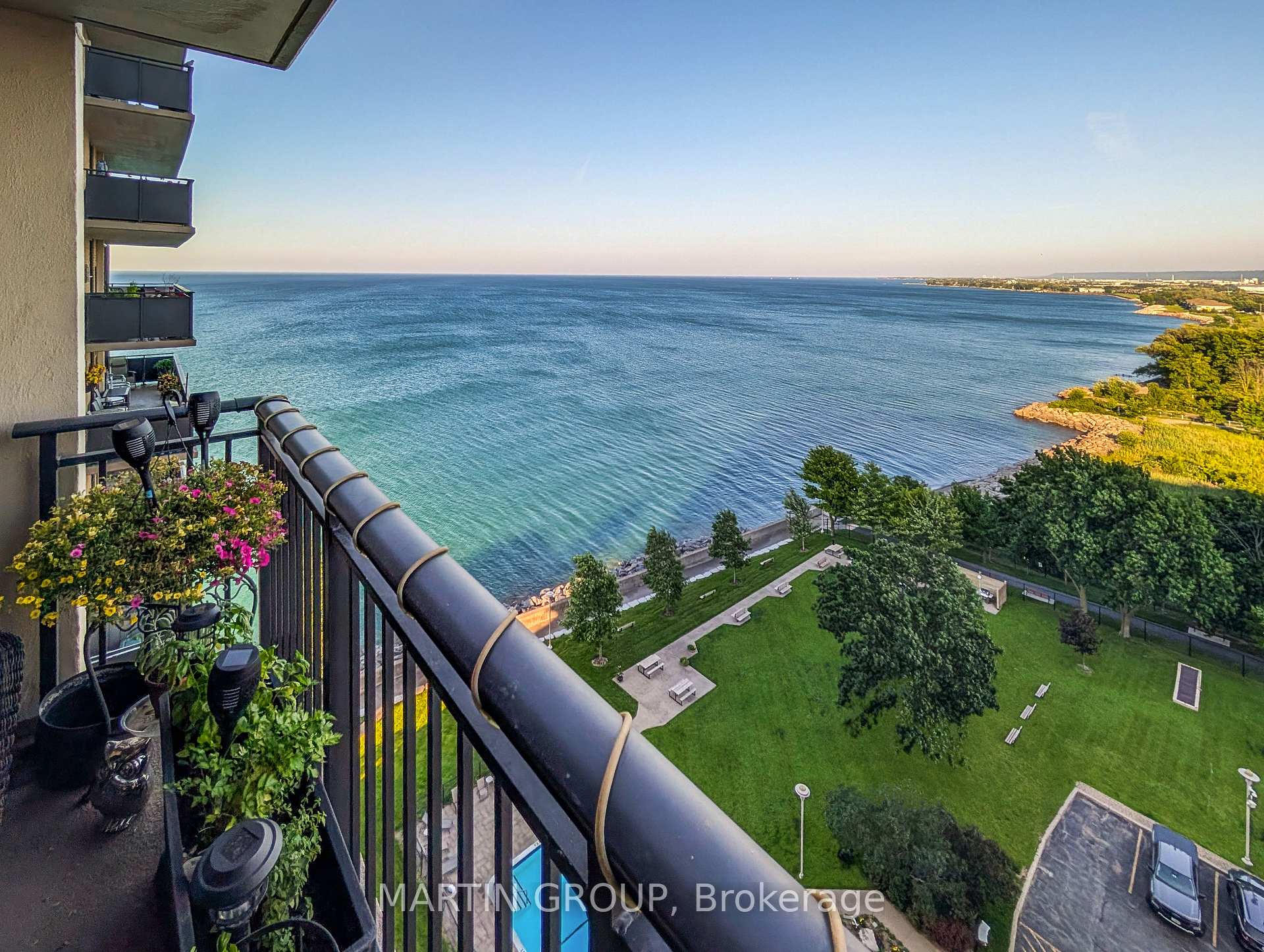 Apartment balcony overlooking the lake and landscaped grounds, with flower planters along the railing.