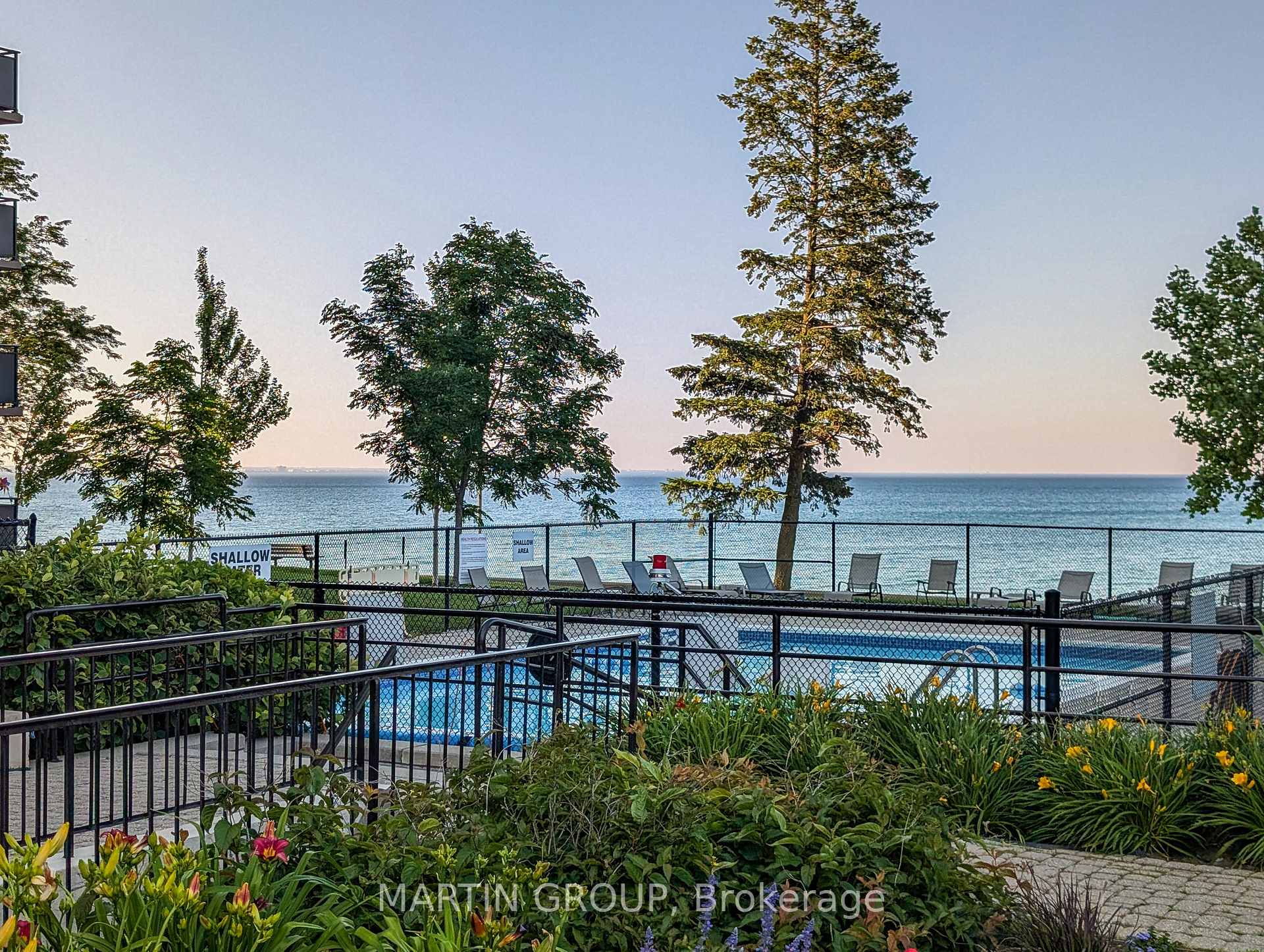 Condominium pool beside the lake, framed by trees and flower beds.