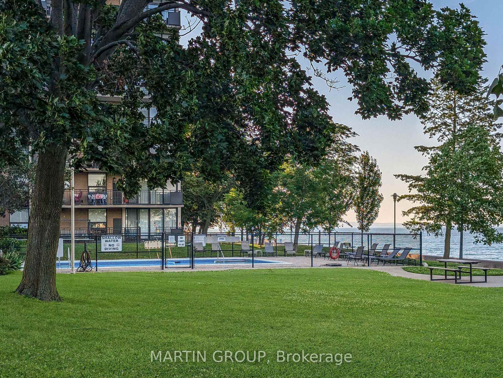 Condominium grounds with a fenced pool, mature trees, patio seating, and lakefront views.