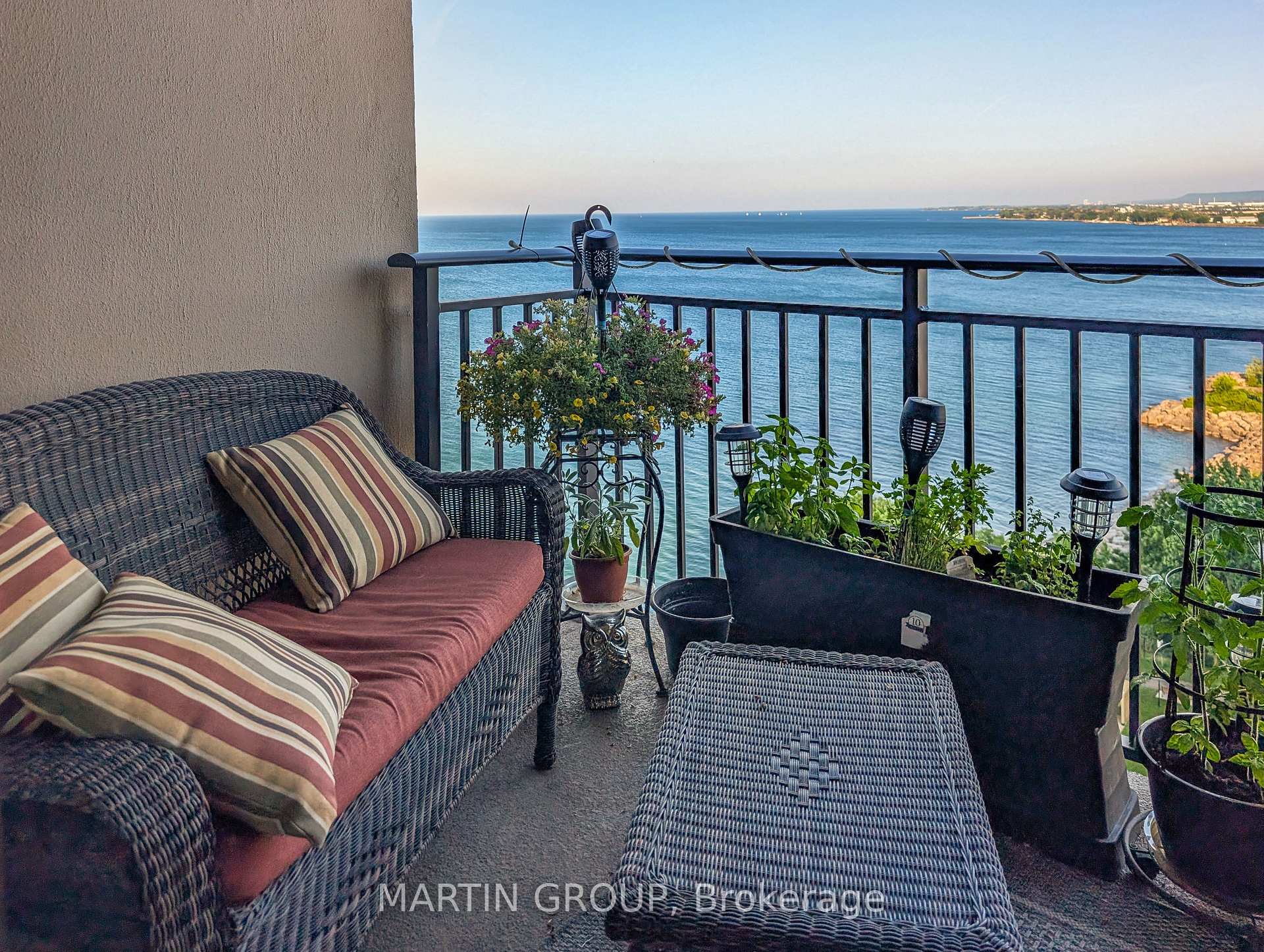 Furnished balcony with wicker seating and potted plants overlooking the water.