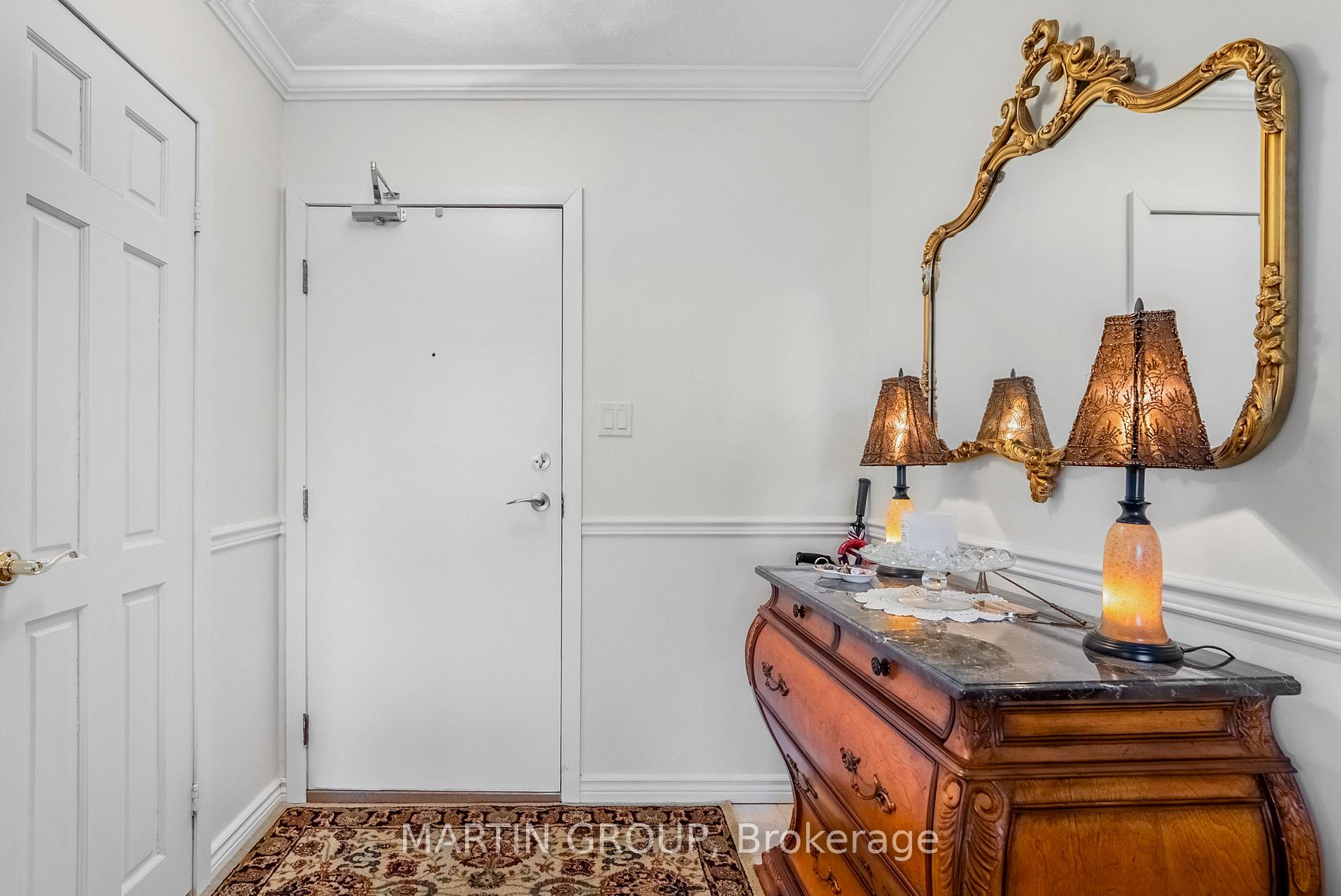 Condo entryway with an ornate wooden console, gold-framed mirror, and patterned rug.