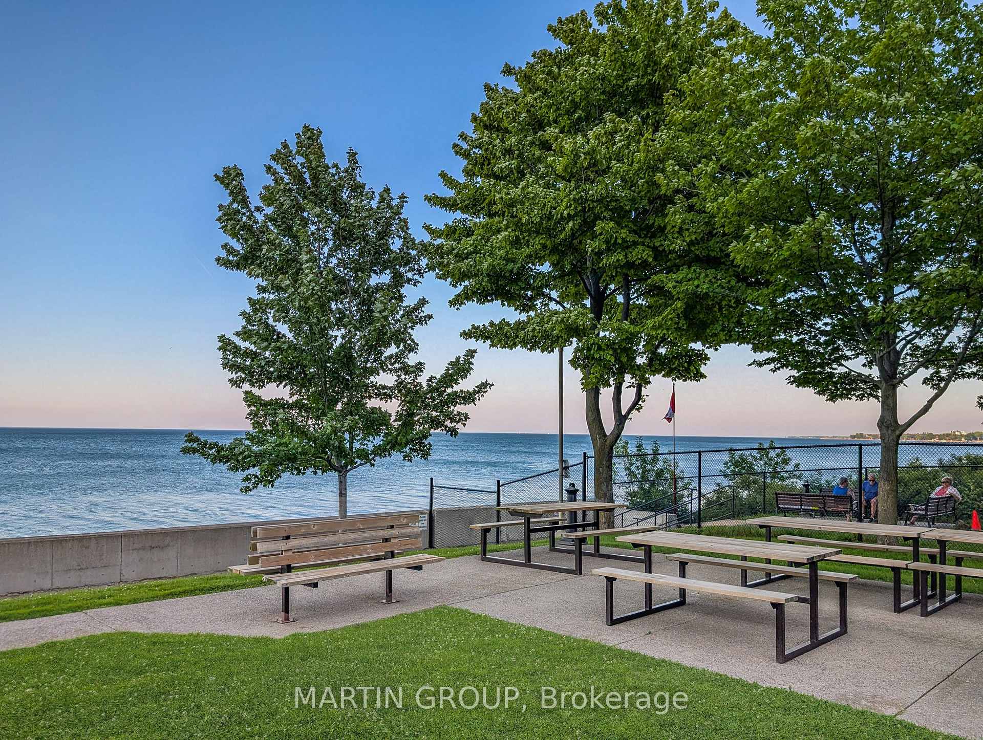 Waterfront picnic area with benches and tables beneath trees beside the lake.