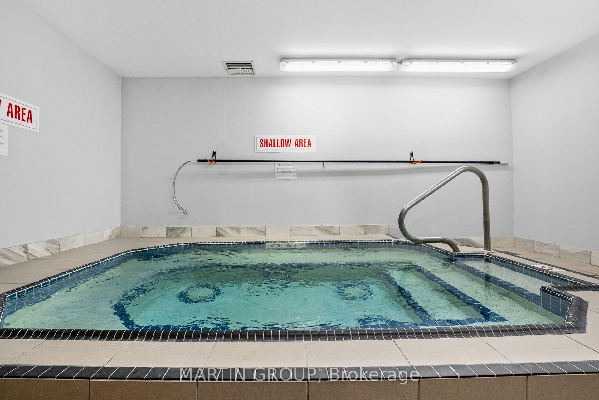 Indoor swimming pool with tiled edges and a metal handrail beside a shallow-area sign.
