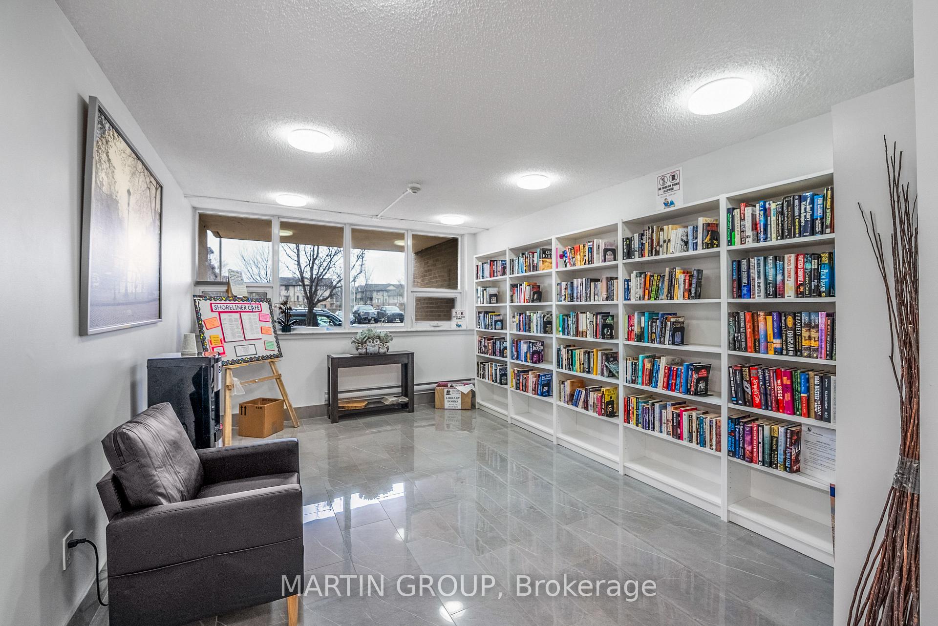Common-area library with book-filled shelves, a dark armchair, and large windows.