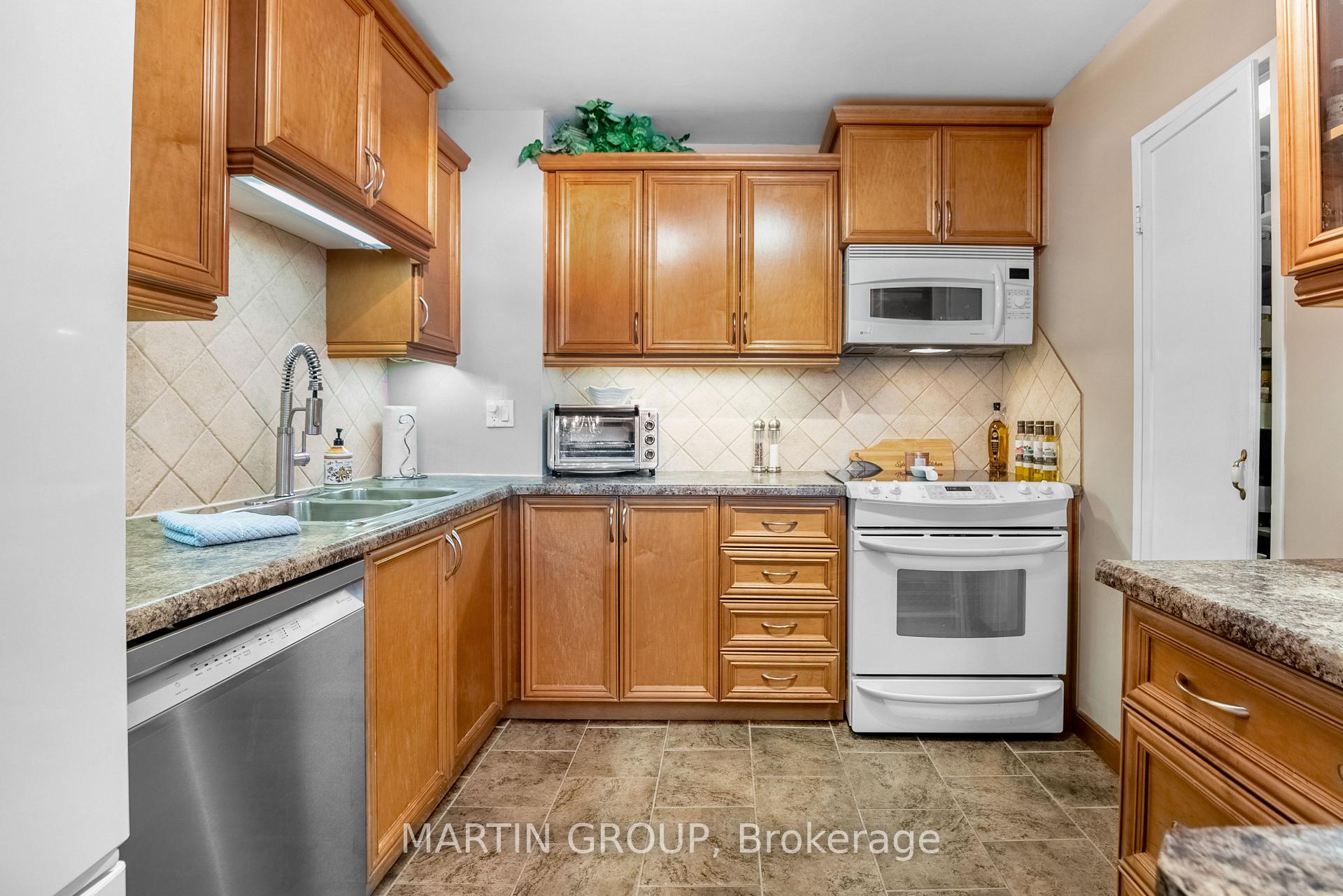 Kitchen with honey-toned wood cabinets, tiled backsplash, and white range and microwave.