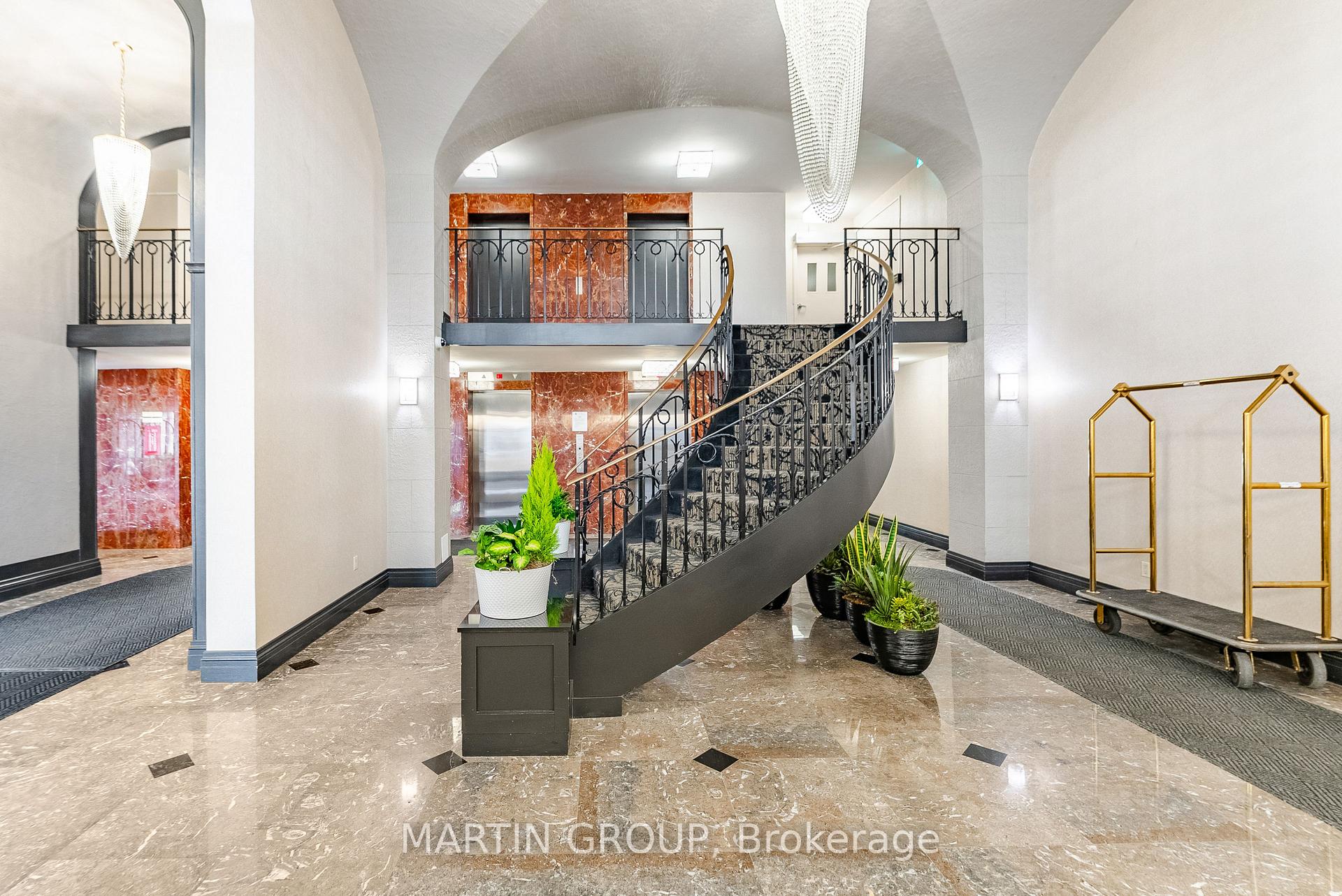Condominium lobby with a curved staircase, ornate railings, marble floors and elevator doors.