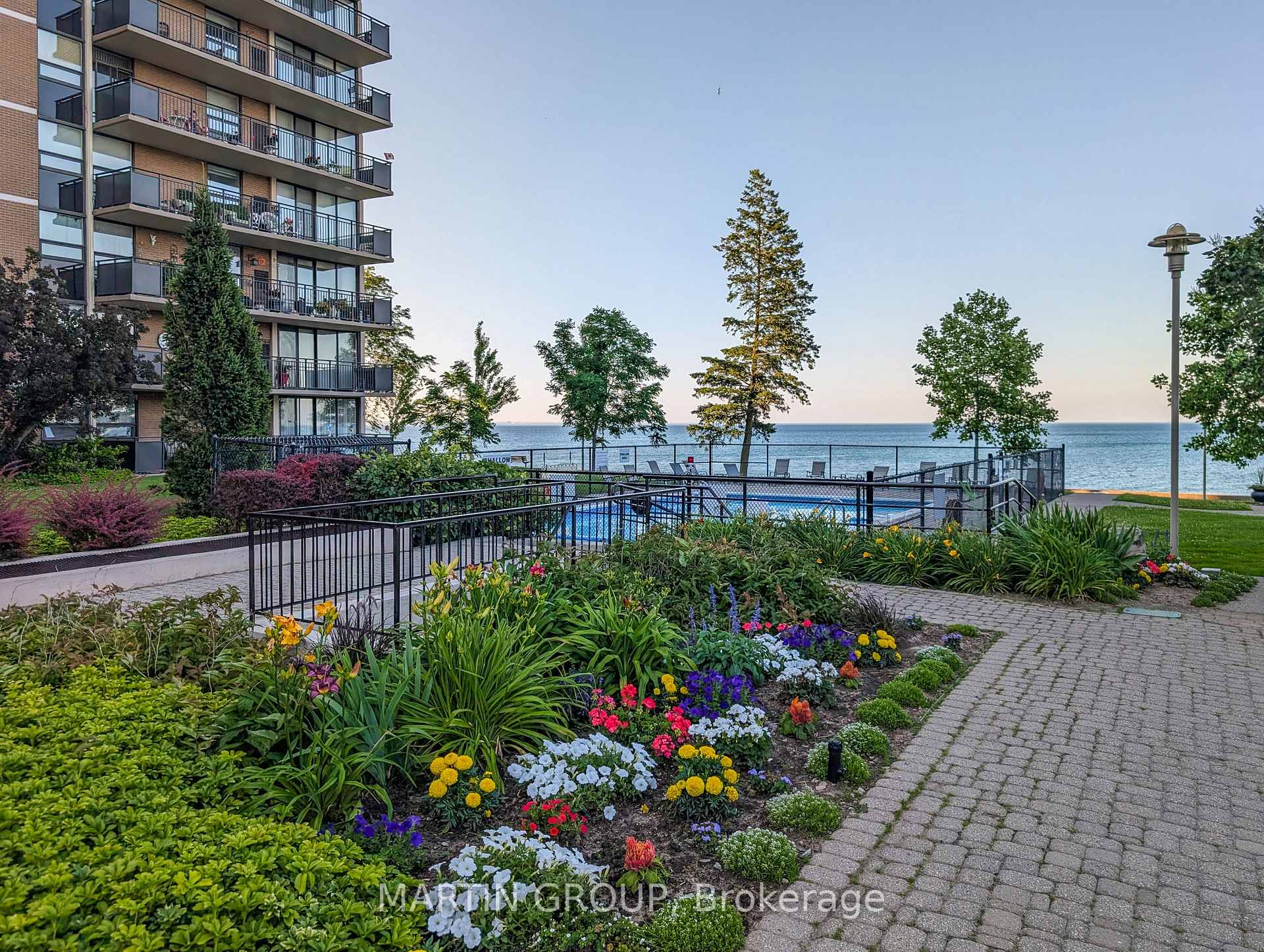 Waterfront condominium grounds with a pool, colorful flower gardens, and balconies overlooking the water.