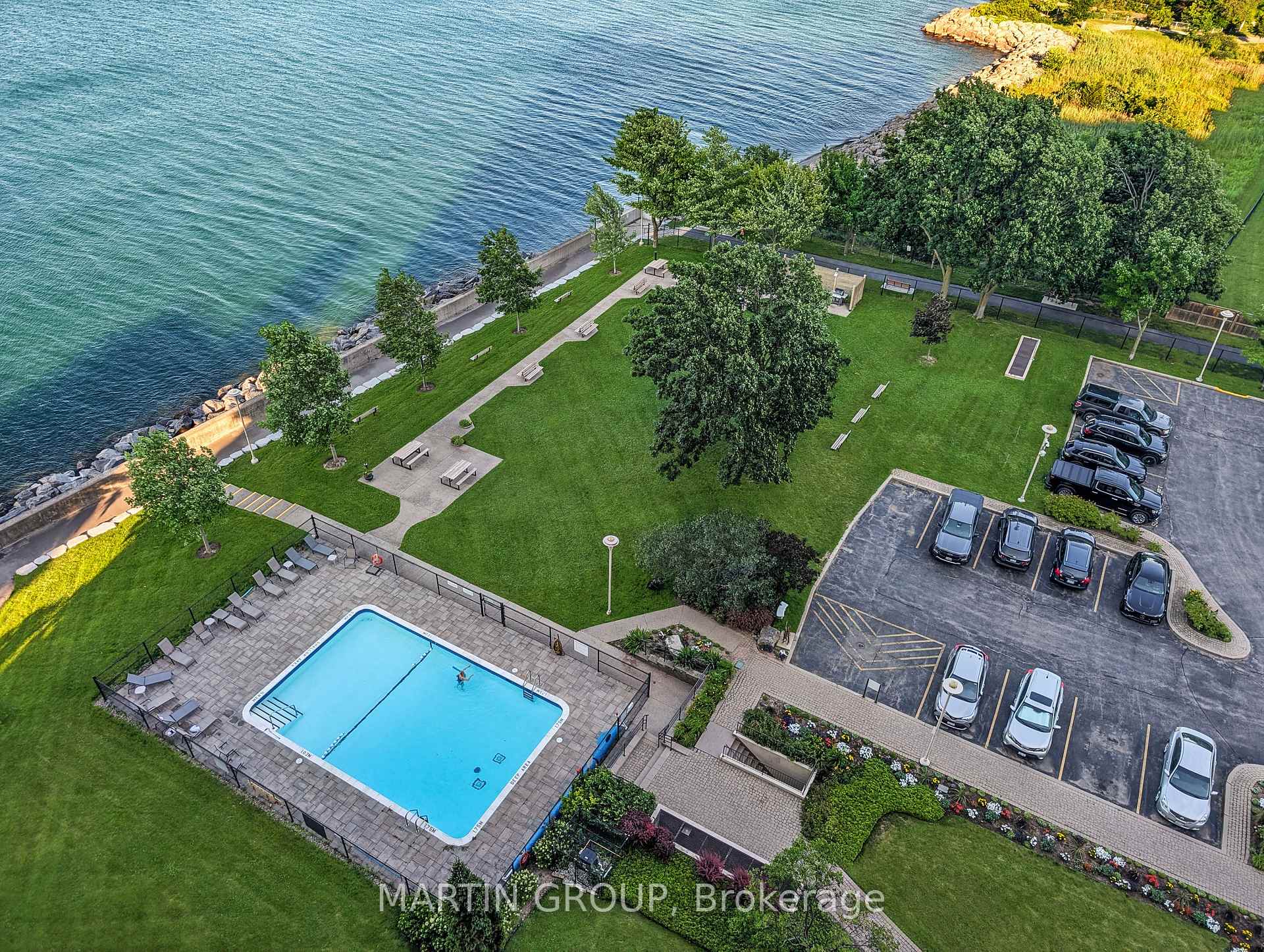 Waterfront condominium grounds with an outdoor pool, landscaped lawn, and shoreline.