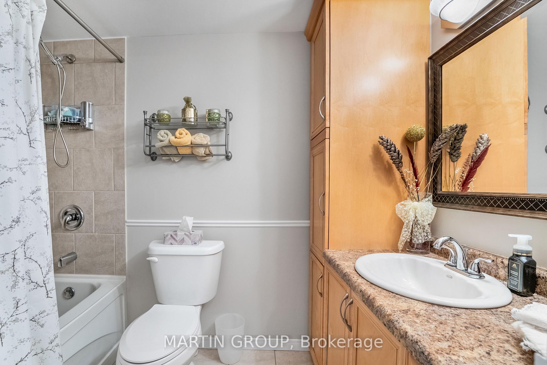 Bathroom with tiled tub and shower, wood vanity, granite countertop, and large framed mirror.