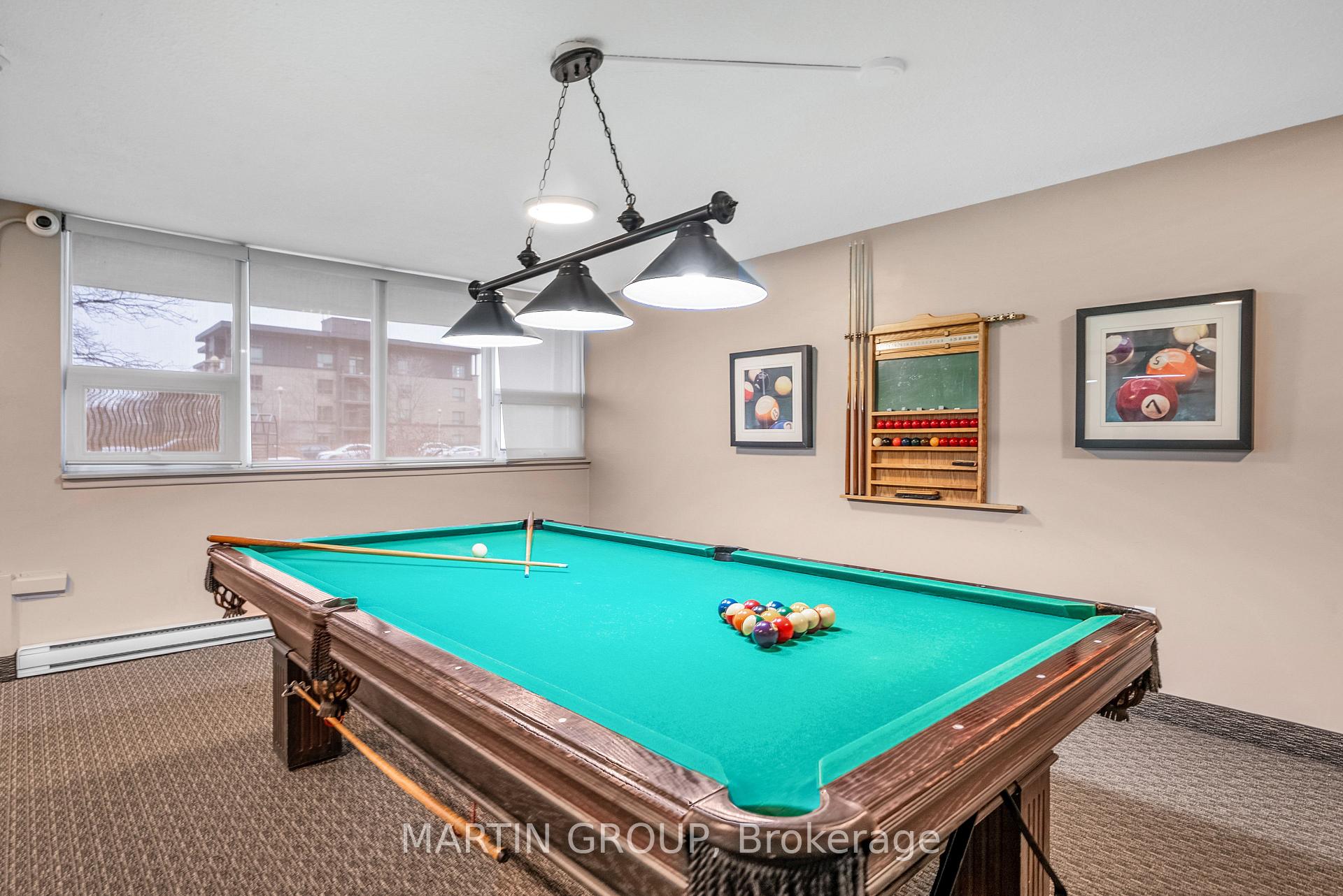 Furnished billiard room with a green-felt pool table and wide windows.