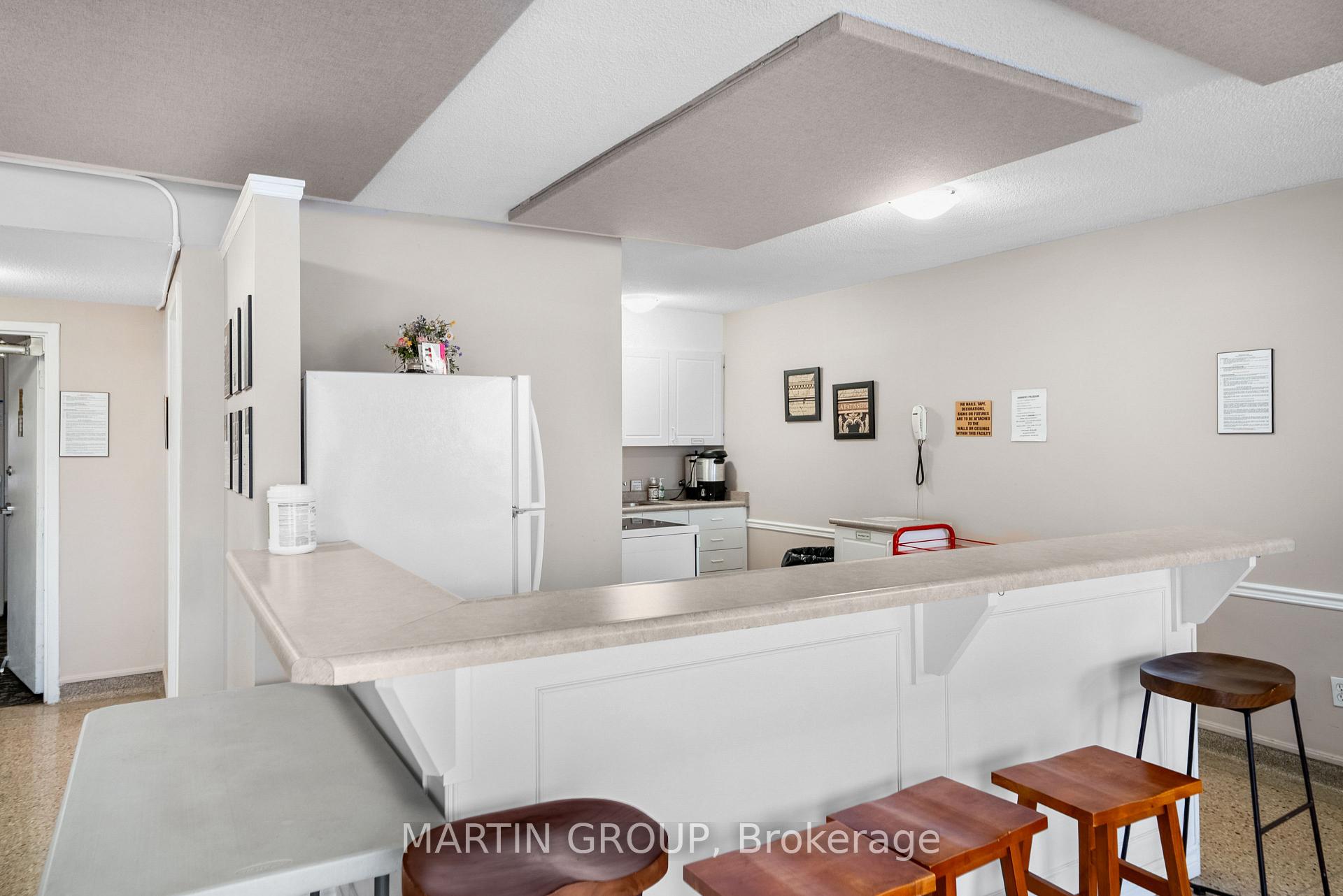 Shared kitchenette with a long counter, bar stools, refrigerator, and compact kitchen area.