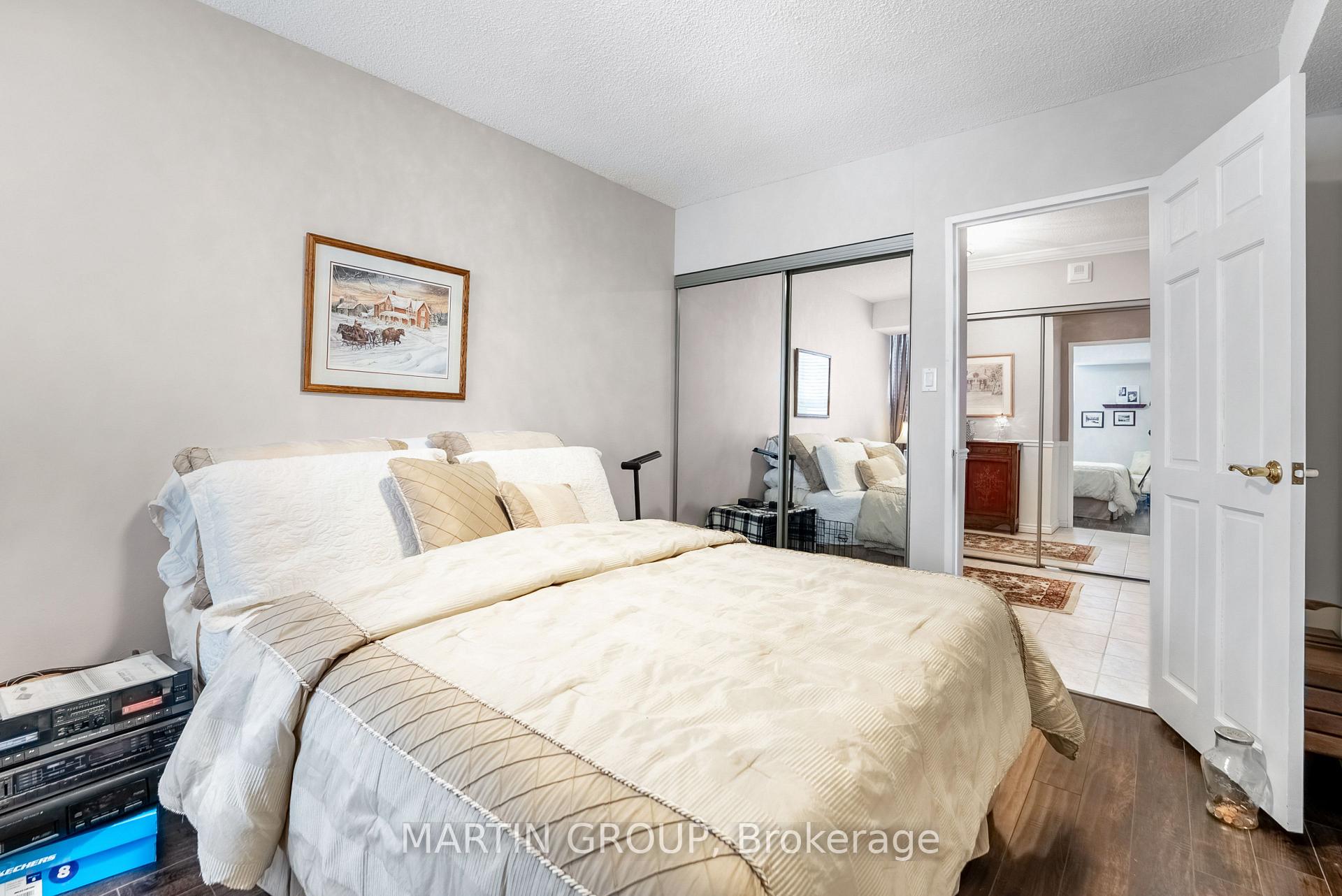 Furnished bedroom with a large cream-and-white bed, mirrored closet doors, and an open doorway.