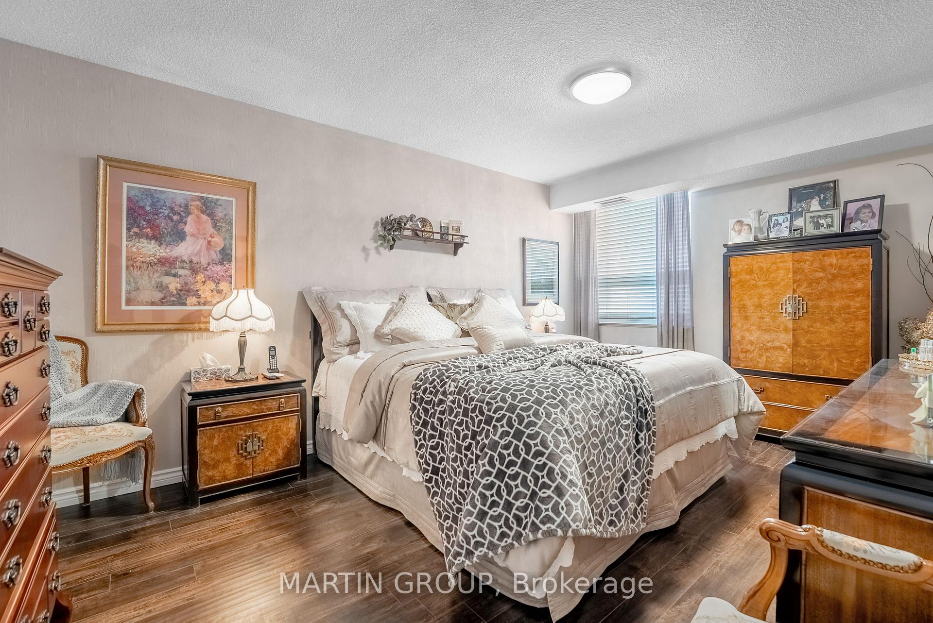 Furnished bedroom with a large bed, patterned blanket, dark wood floors, and warm-toned wood furniture.