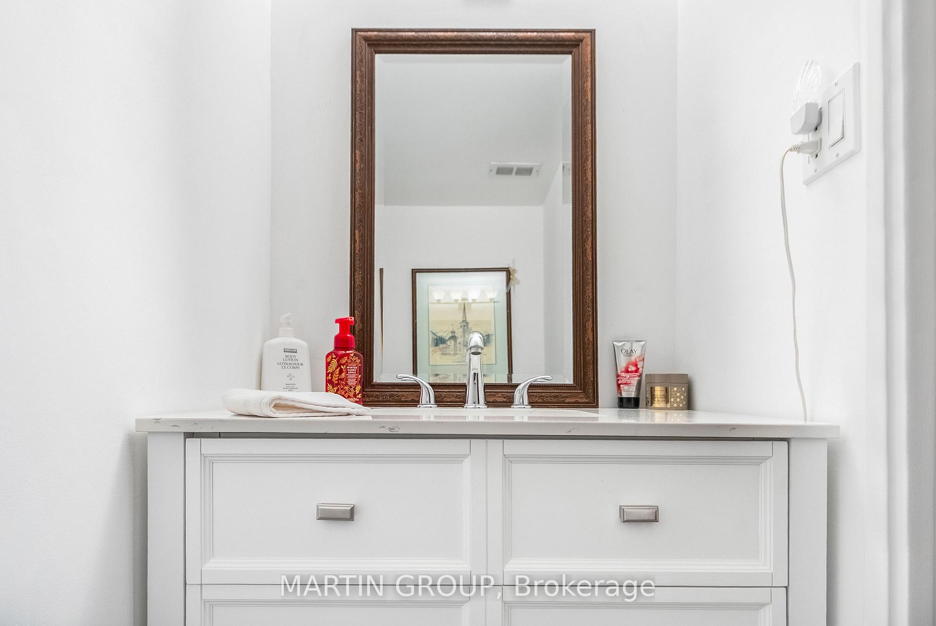 White bathroom vanity with chrome faucet, ornate framed mirror, toiletries and a folded towel.