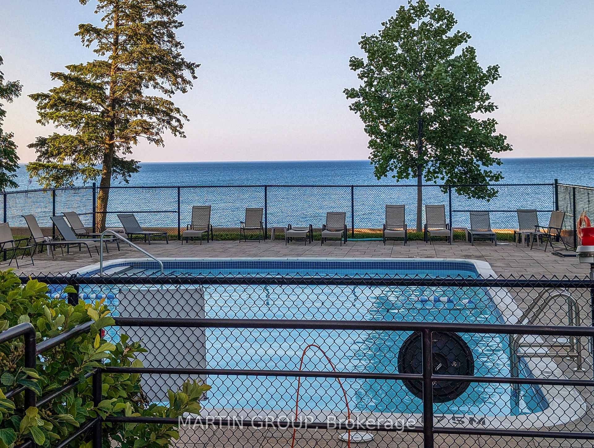 Outdoor swimming pool overlooking the water, with patio chairs along the fence.