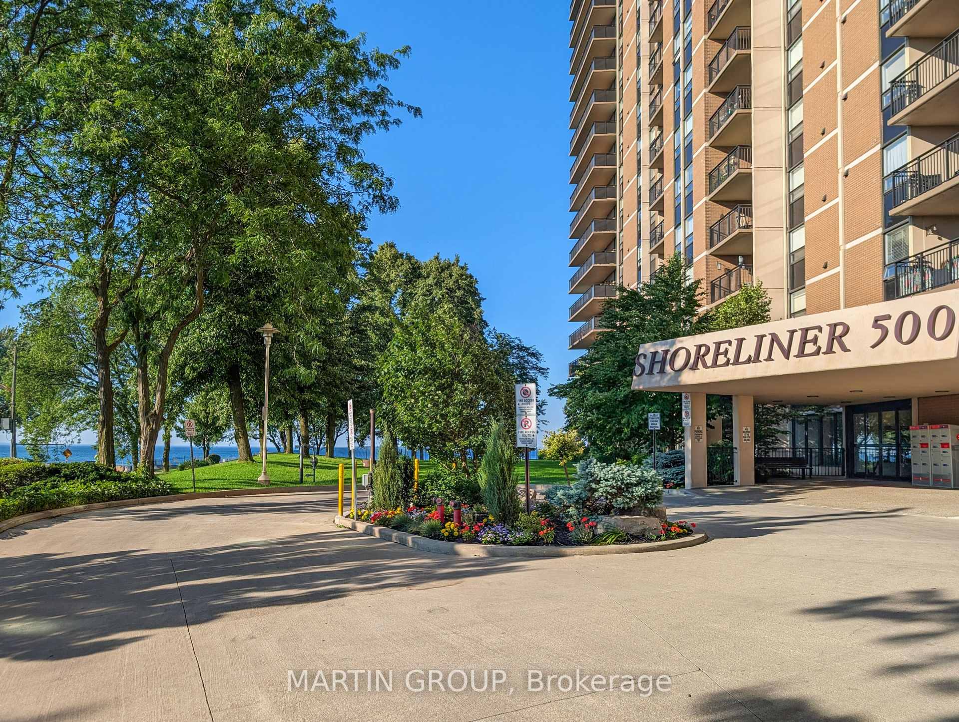 Shoreliner 500 condominium entrance beside landscaped grounds and a tree-lined waterfront.