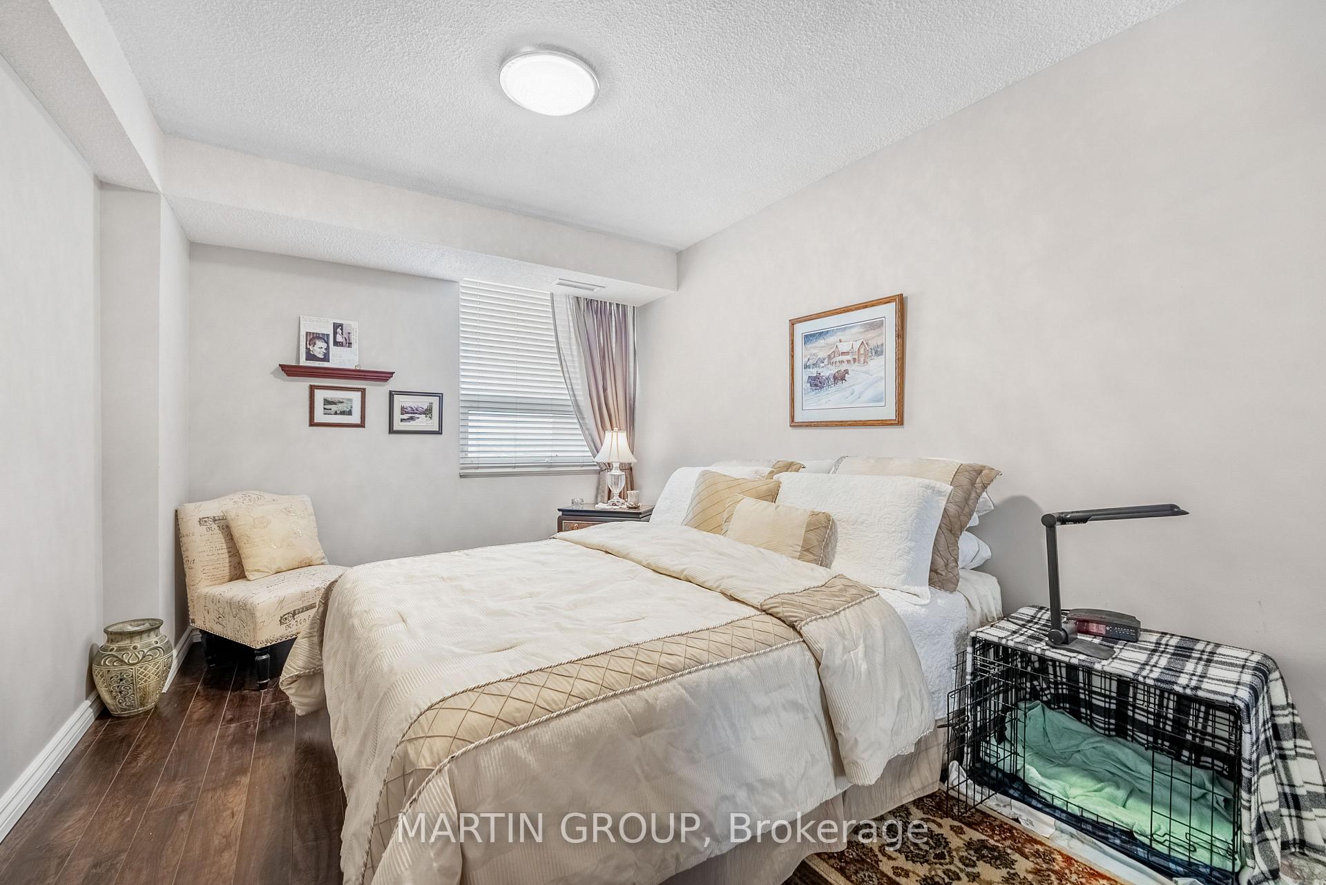 Furnished bedroom with a cream-covered bed, window blinds, framed art, and a covered pet crate.