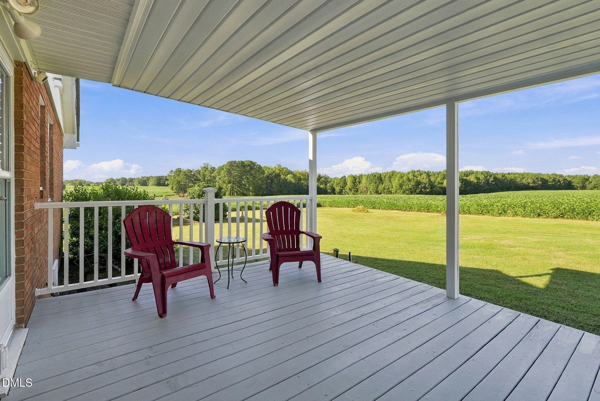 Covered porch with two red Adirondack chairs overlooking a lawn, fields, and tree line.