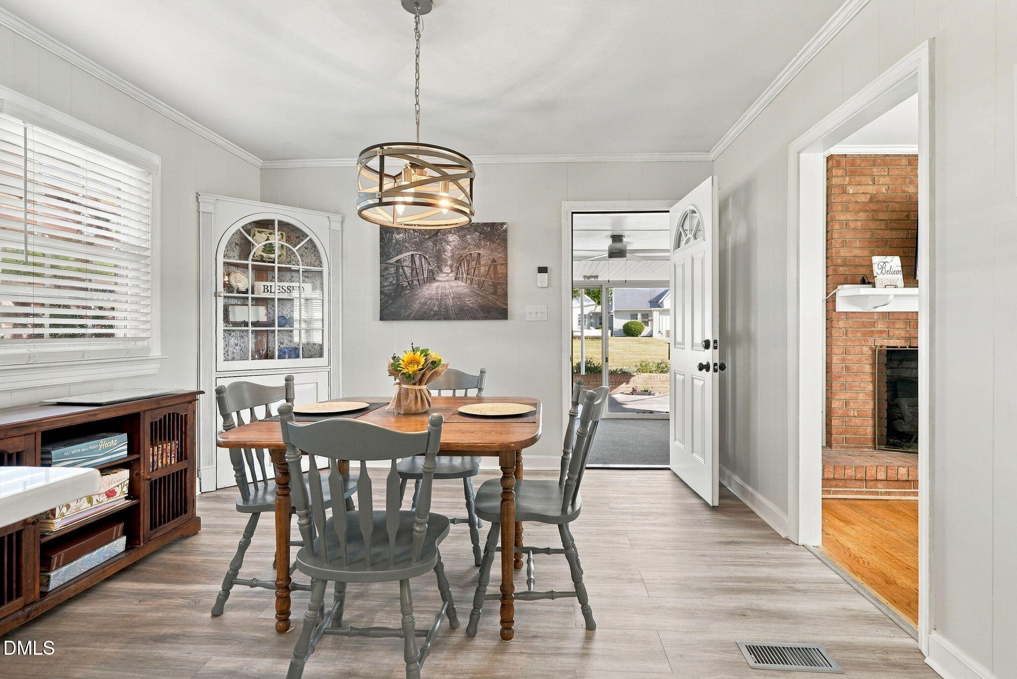 Dining room with a wooden table, gray chairs, china cabinet, and view through the open front door.