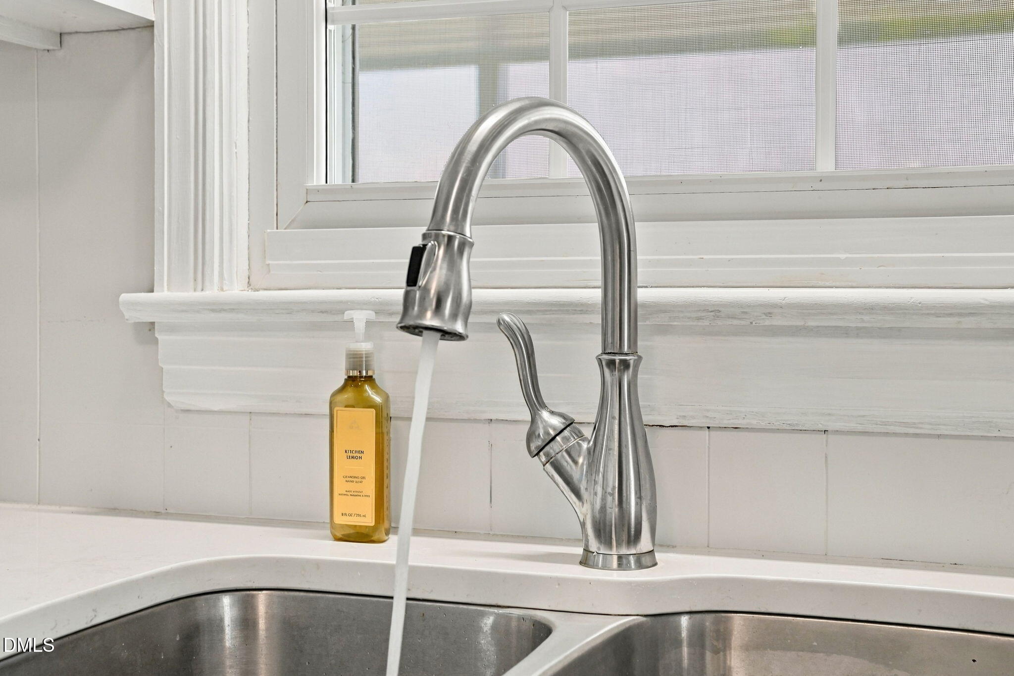 Stainless steel pull-down kitchen faucet running over a double-basin sink beneath a window.