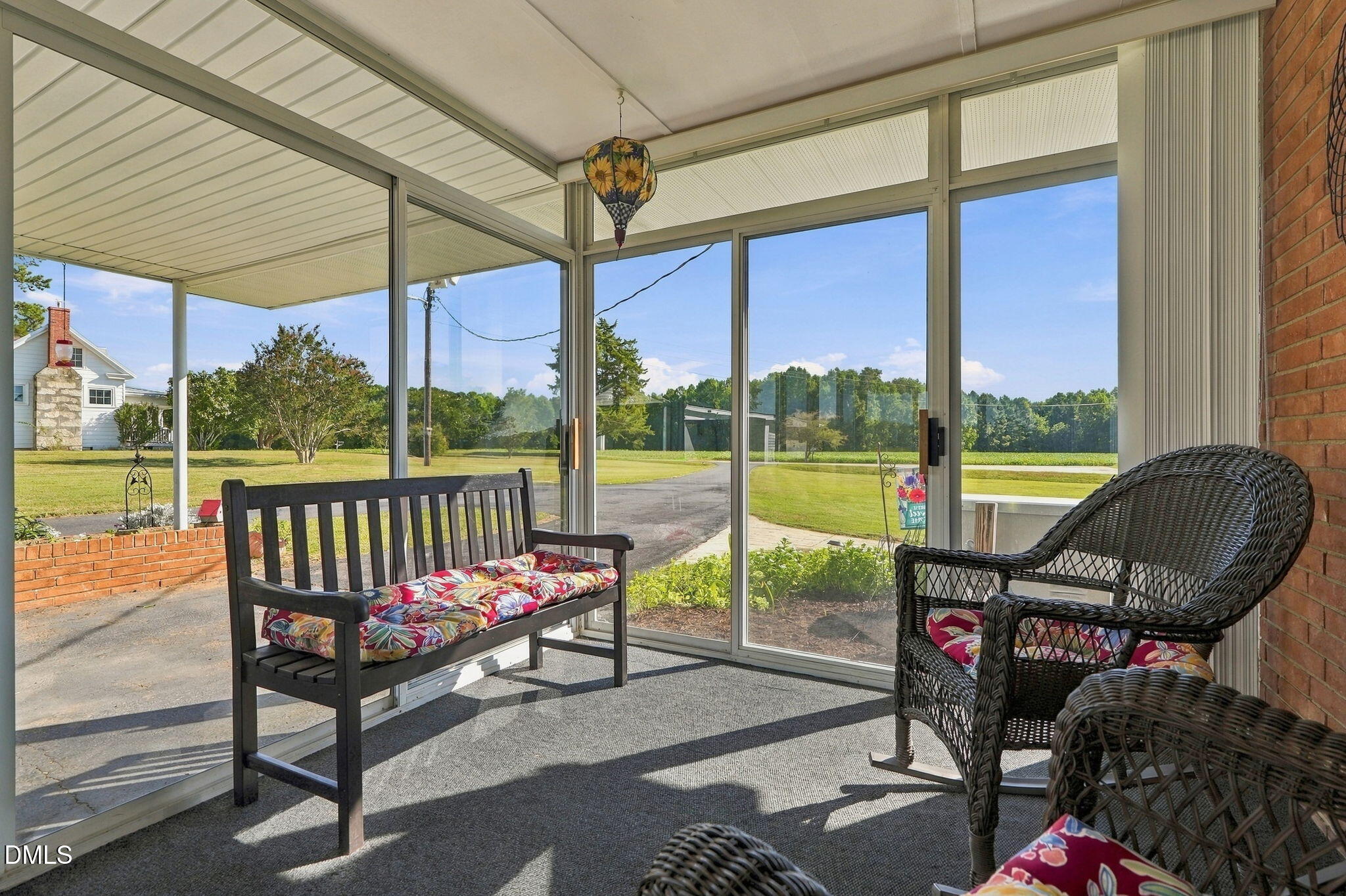 Enclosed sunroom with glass walls, wicker seating, a wooden bench, and views of the lawn.