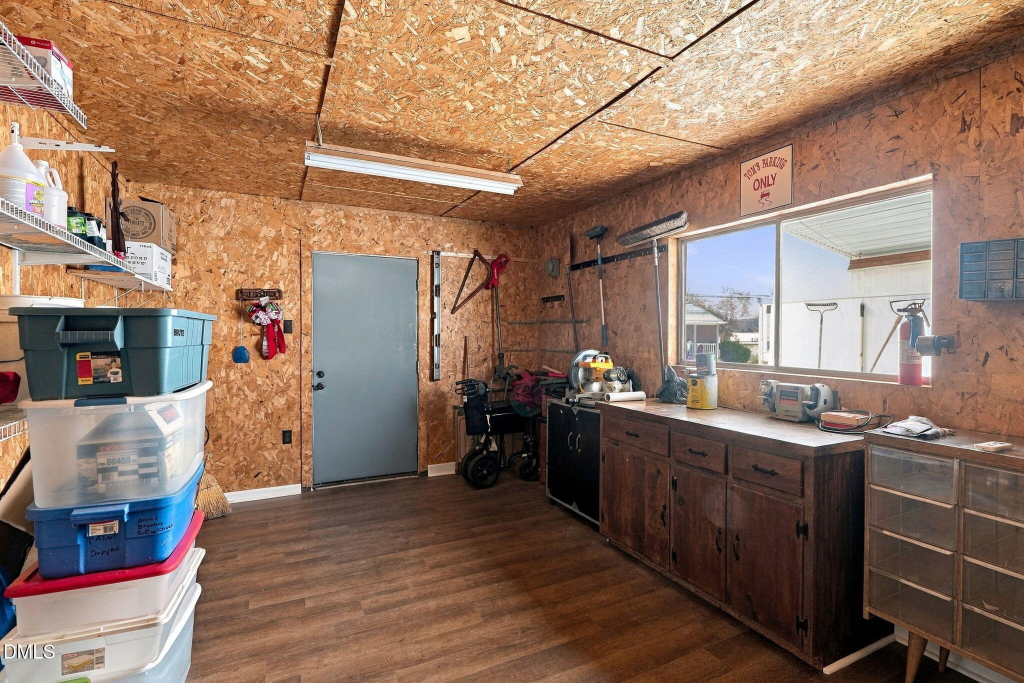 Garage workshop with stacked storage bins, tools, and a long workbench beneath a window.