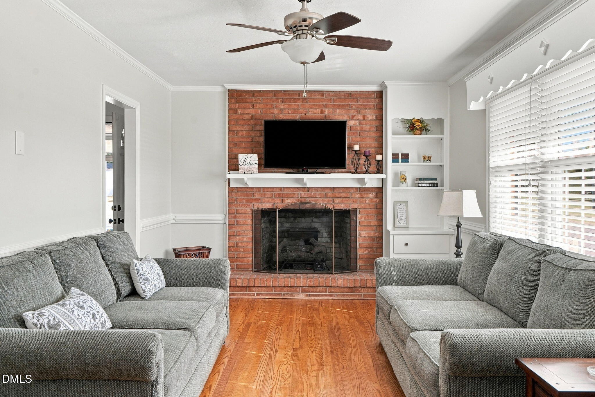 Living room with gray sofas, hardwood floors, and a brick fireplace with a television above it.
