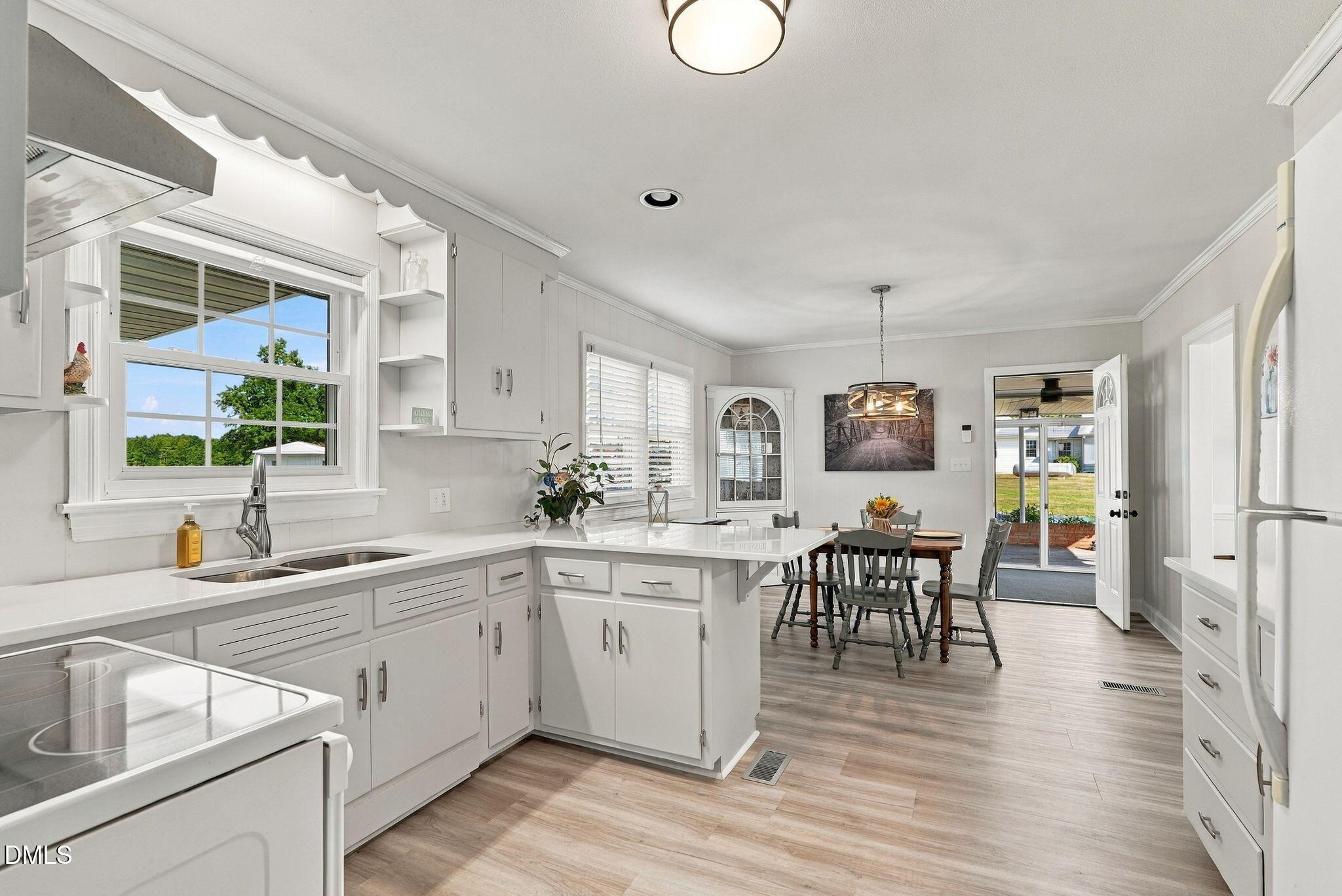 Bright white kitchen with central island, large window, and adjoining dining area opening to the patio.