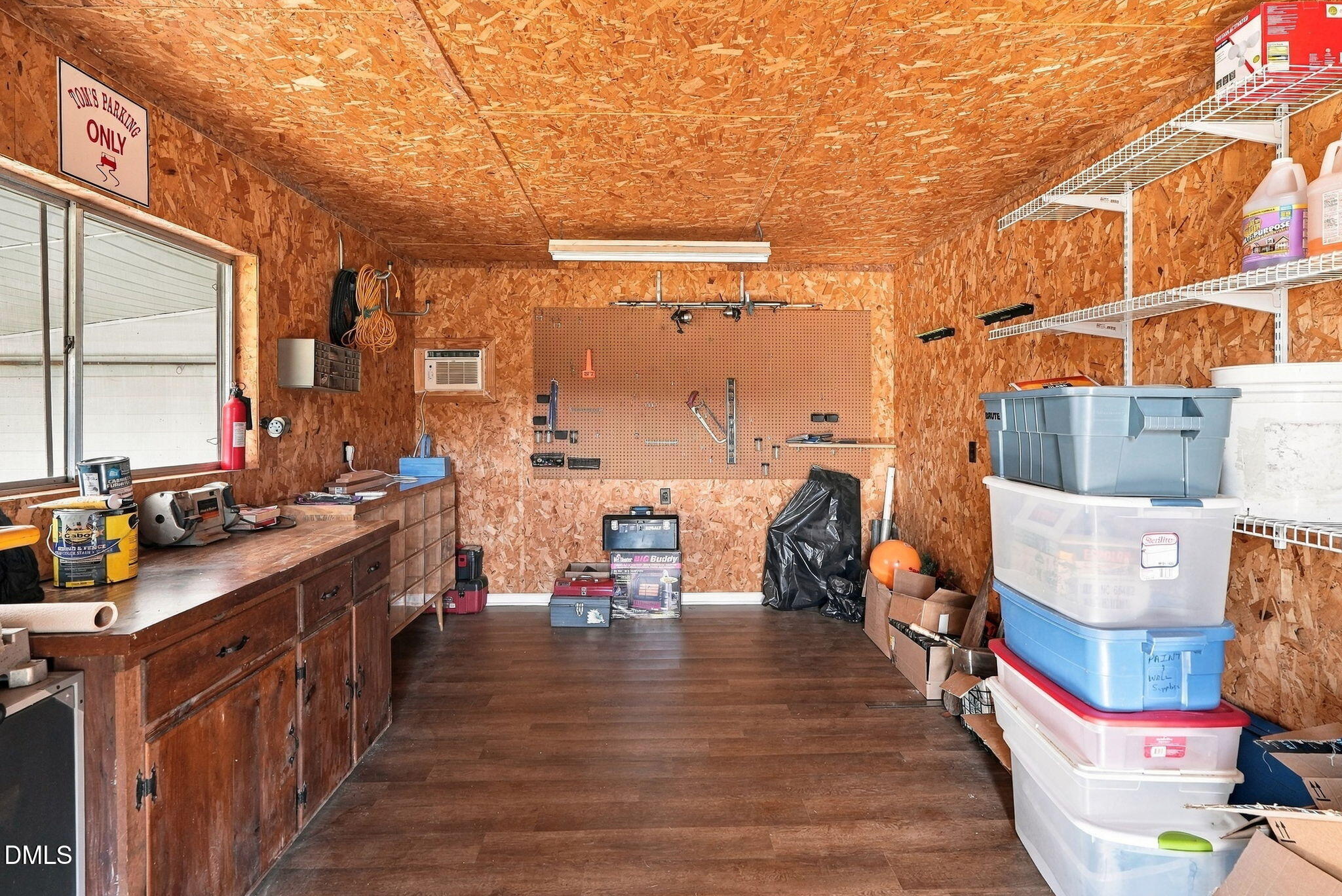 Garage workshop with a long workbench, pegboard tools, wire shelving, and stacked storage bins.