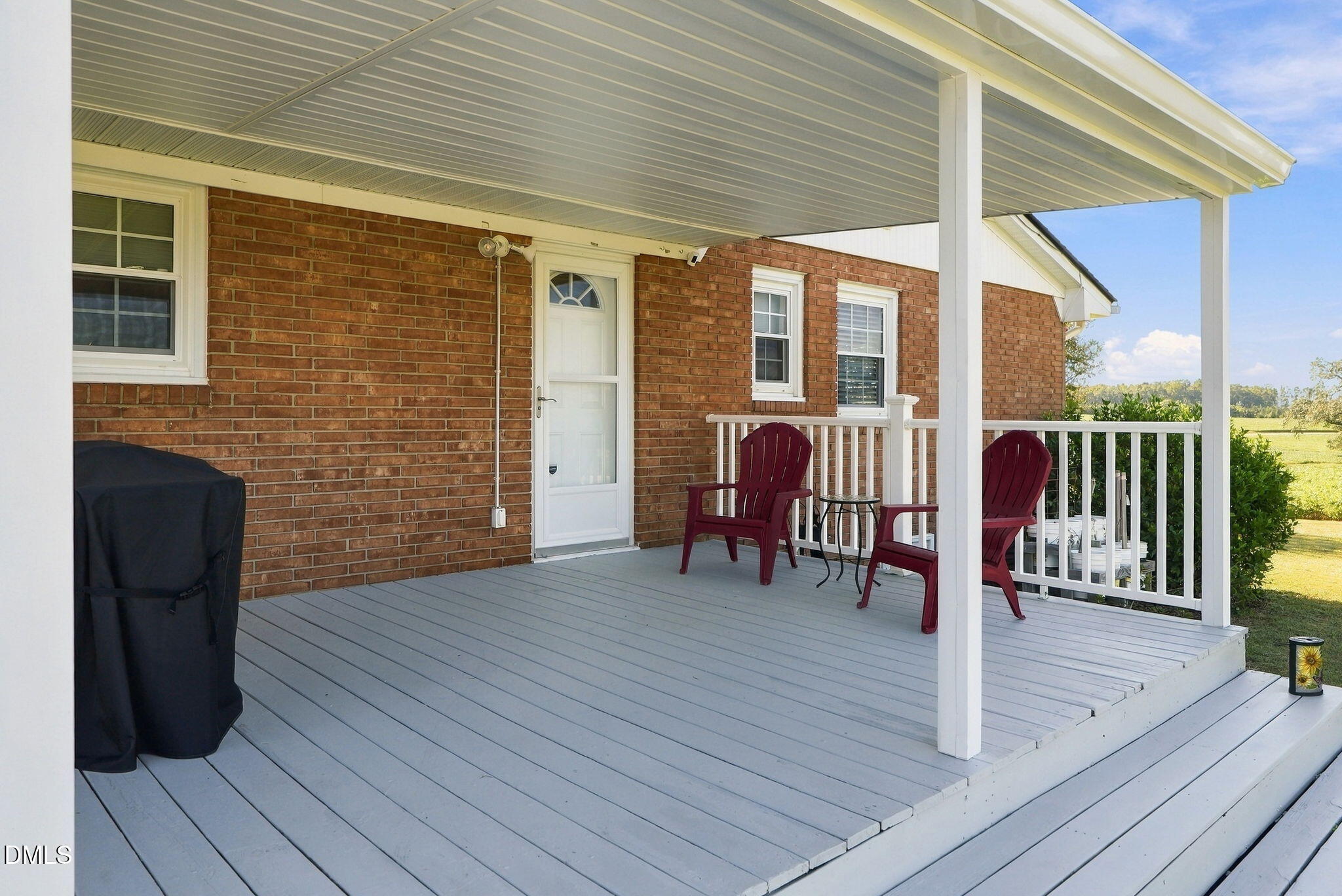 Covered porch with gray decking, burgundy chairs, white railings, and views of open fields.