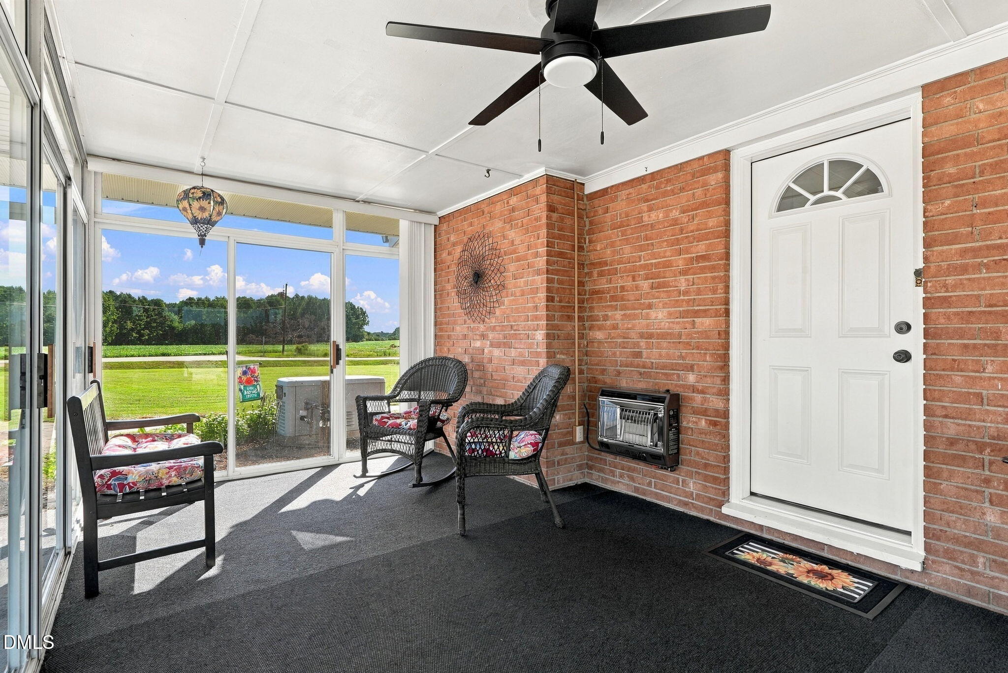 Enclosed porch with brick walls, wicker chairs, and sliding glass windows overlooking green fields.