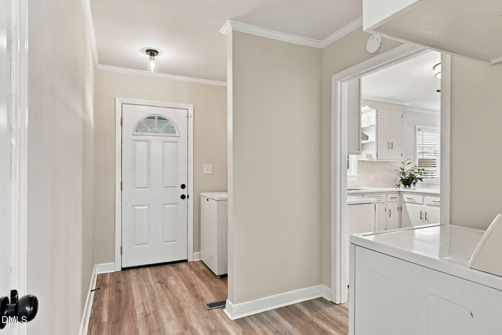 Entryway with a white front door, wood-look flooring, and a view into the kitchen.