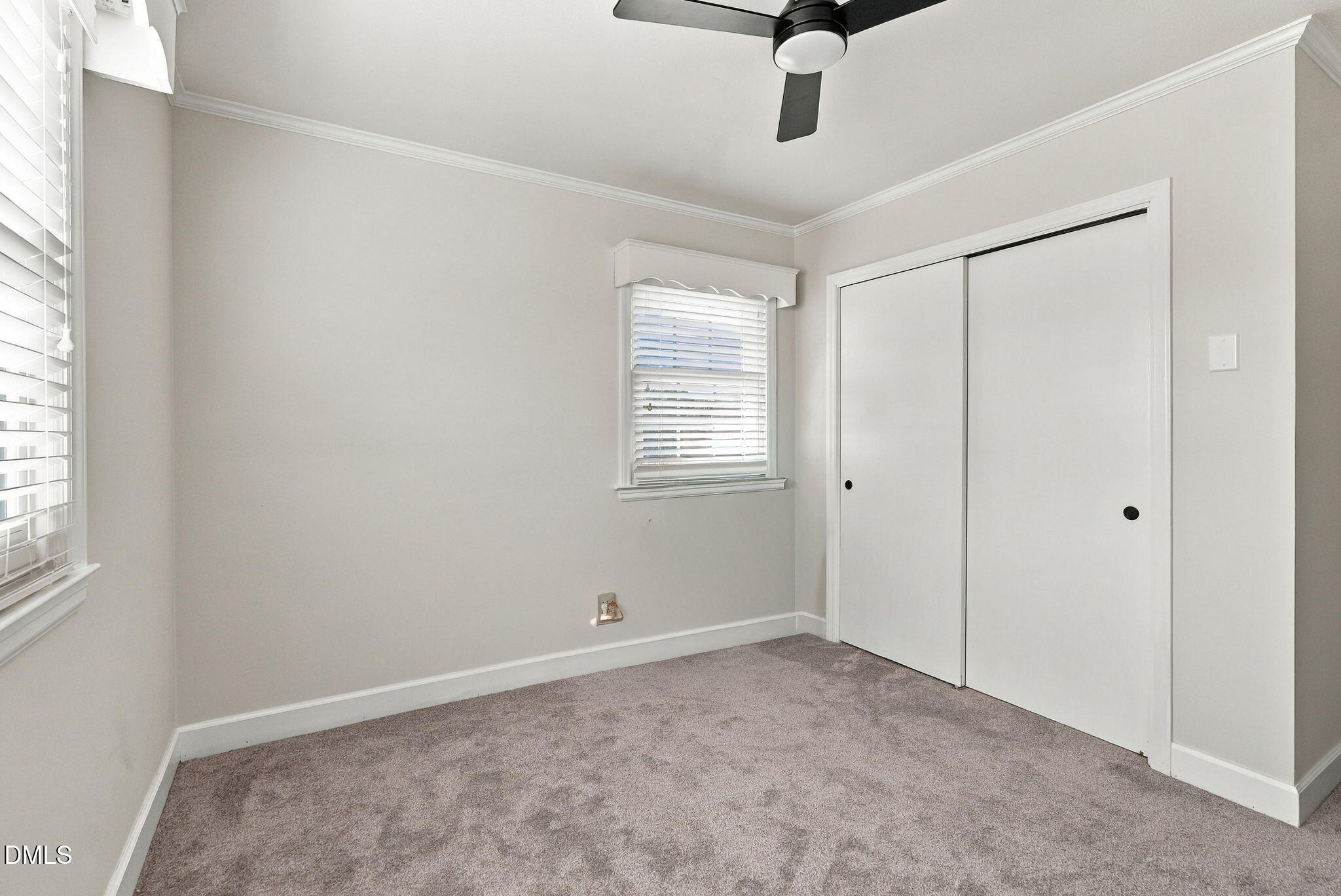 Empty carpeted bedroom with white sliding closet doors, two windows, and a ceiling fan.