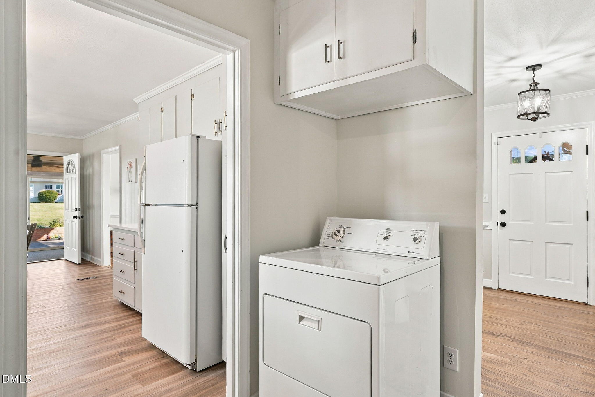 Laundry area with a white dryer, overhead cabinets, and a refrigerator in the adjoining kitchen.