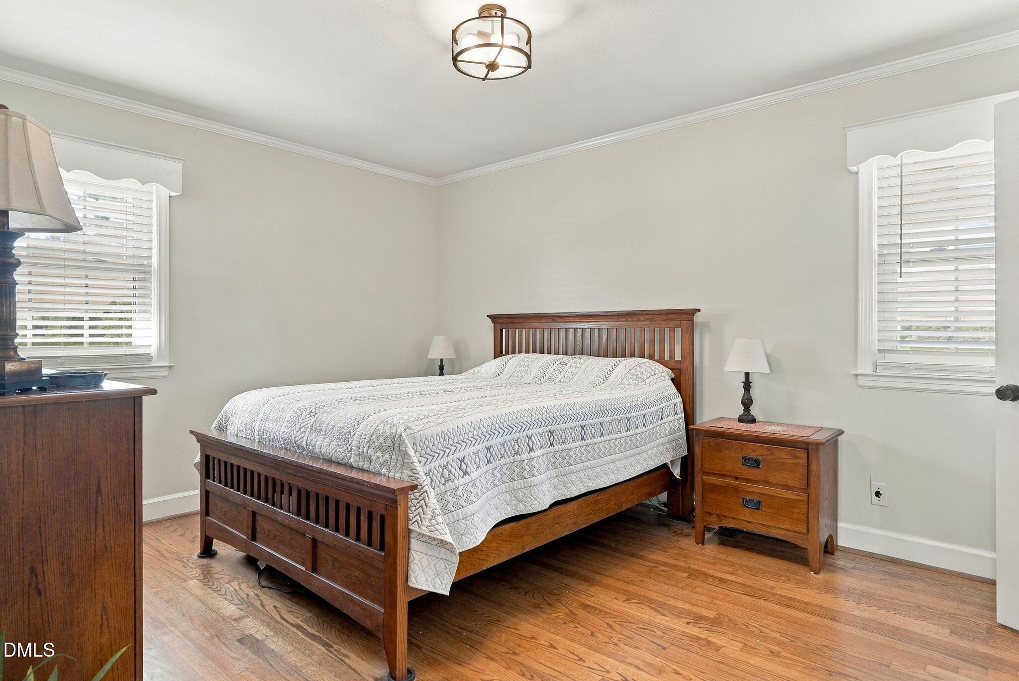 Bedroom with a wooden bed, patterned white quilt, matching nightstands, and hardwood floors.