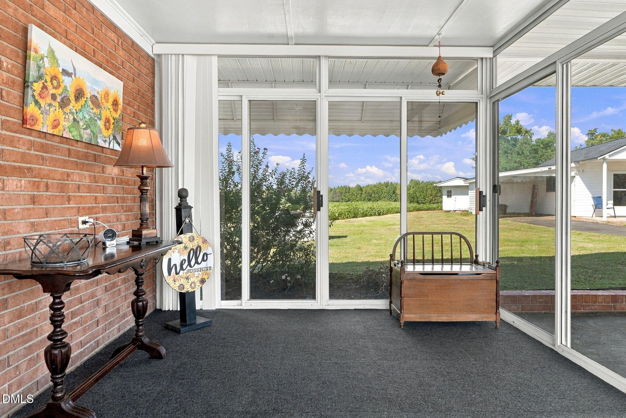 Enclosed sunroom with brick walls, glass doors, and views of a lawn and cornfield.