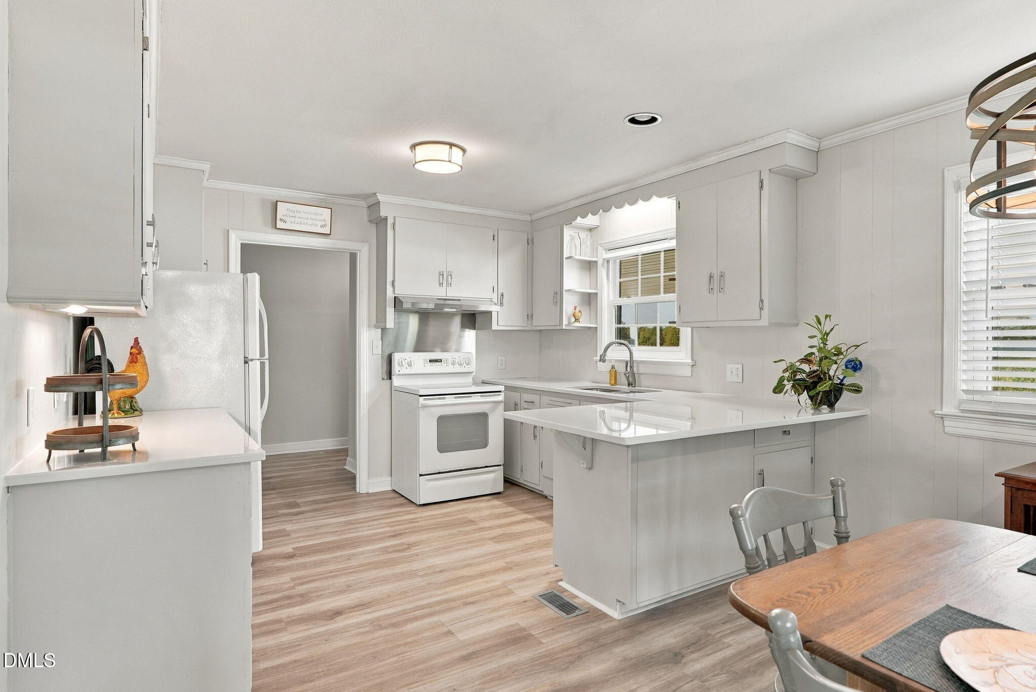 White kitchen with central island, sink beneath a window, and light wood-look flooring.