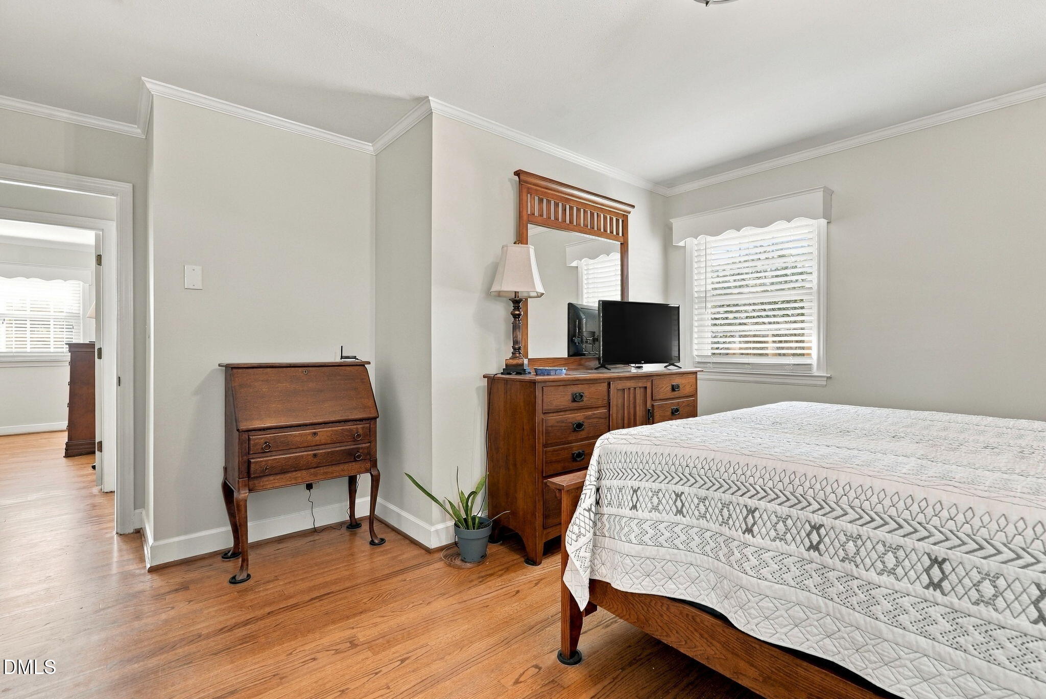 Furnished bedroom with a geometric quilt, wooden dressers, and hardwood floors.