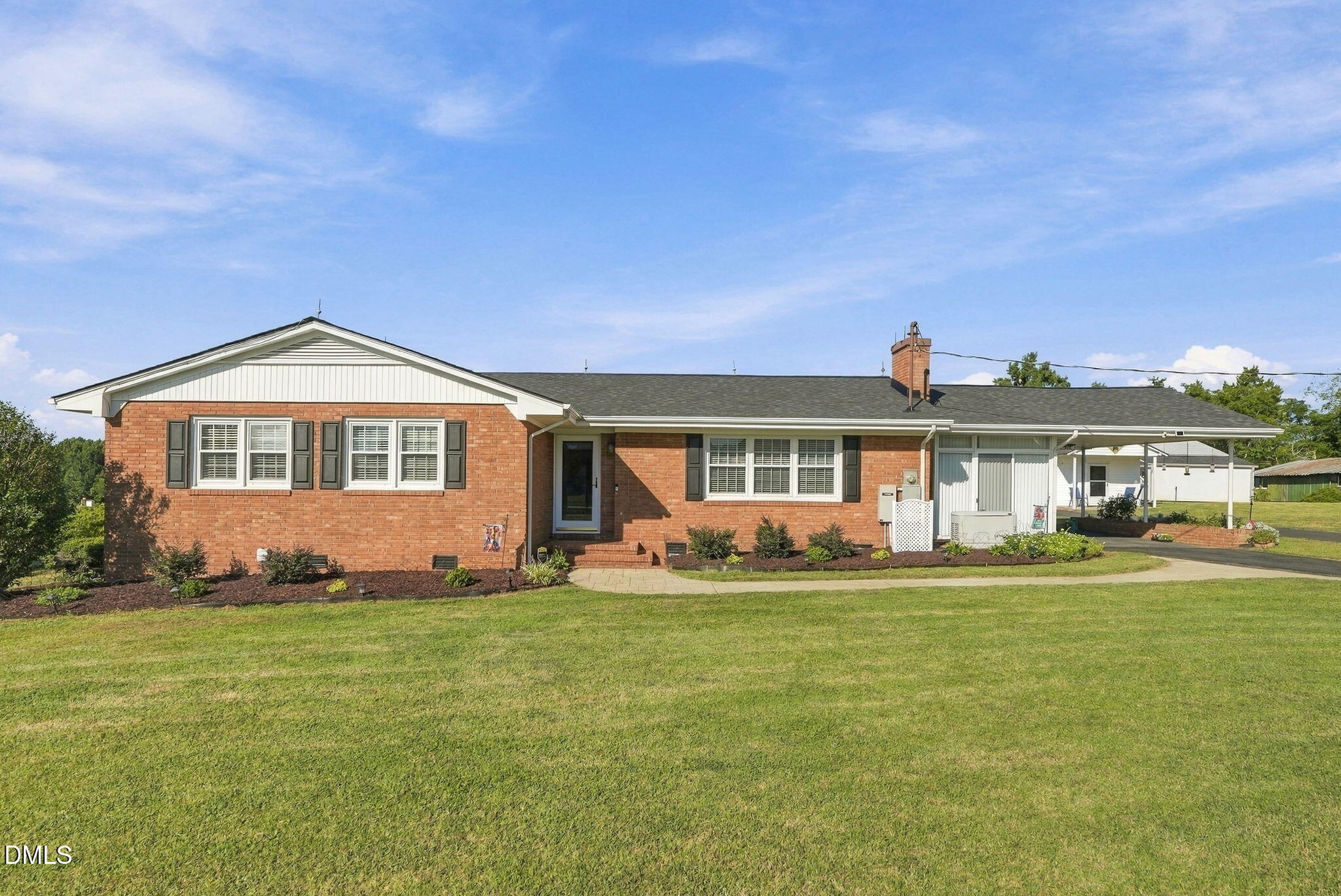 Red brick ranch house with white trim, landscaped shrubs, and a covered carport beside a broad lawn.