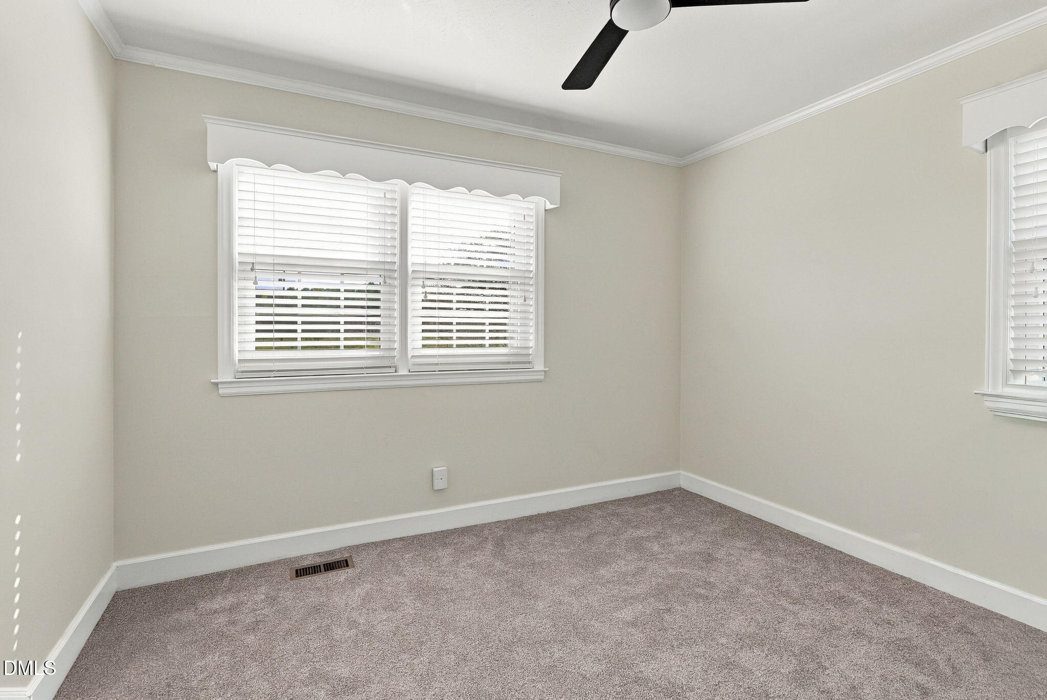 Empty carpeted bedroom with two windows, white blinds, and a black ceiling fan.