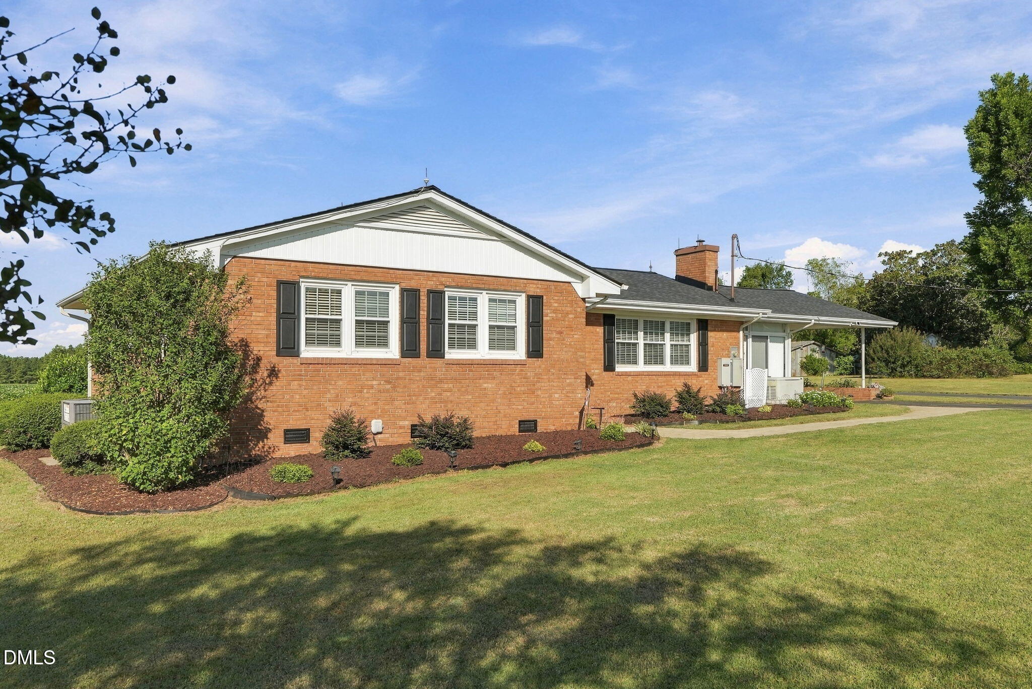 Red brick ranch house with white gables, landscaped foundation beds, and a covered side carport.