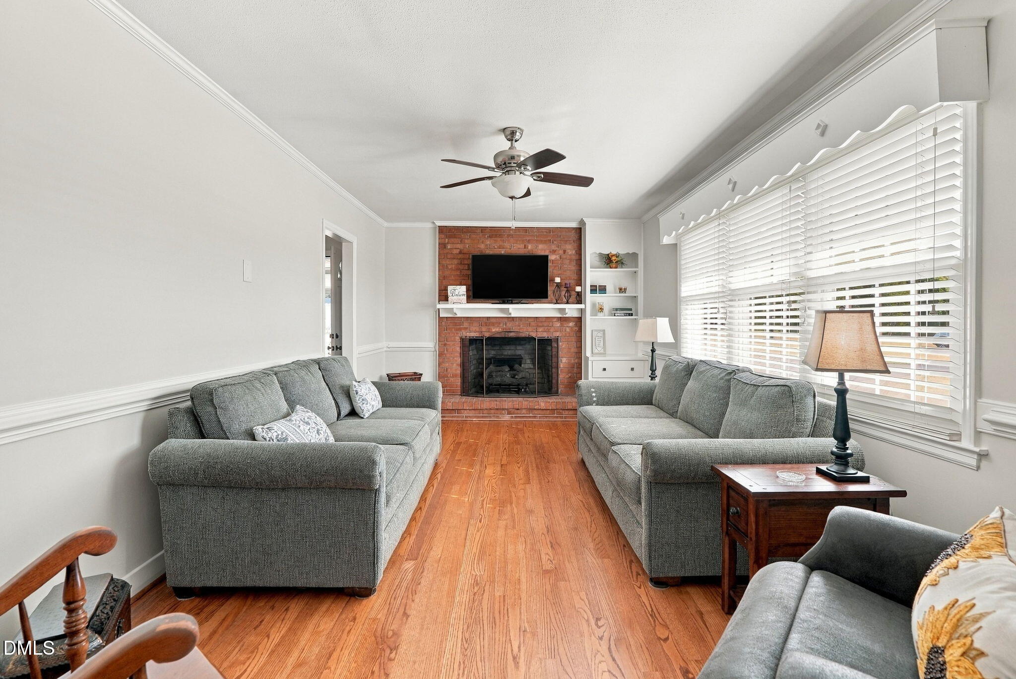 Living room with gray sofas, hardwood floors, and a brick fireplace beneath a wall-mounted television.
