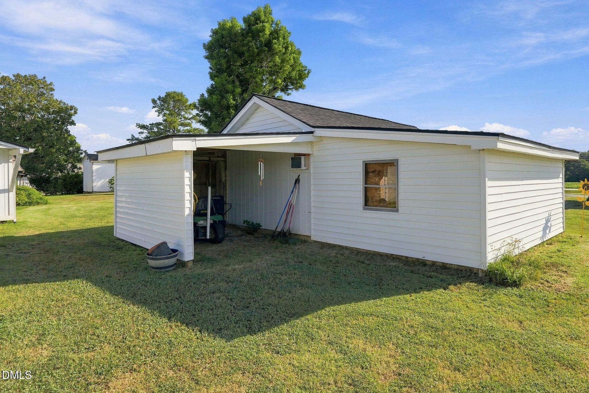White detached outbuilding with a covered open bay beside a grassy yard.
