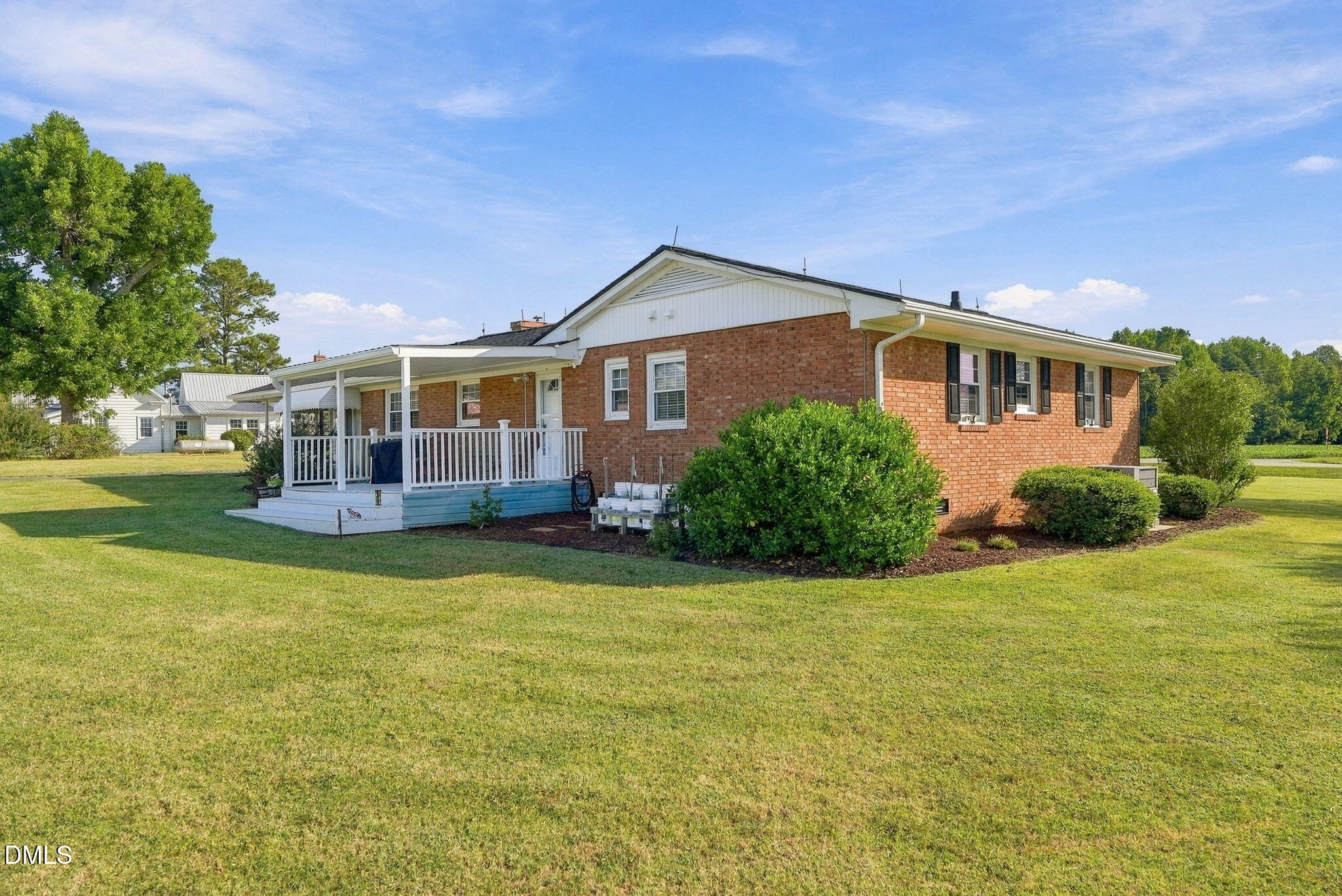 Red brick house with a white covered porch, shrubs, and a broad green lawn.