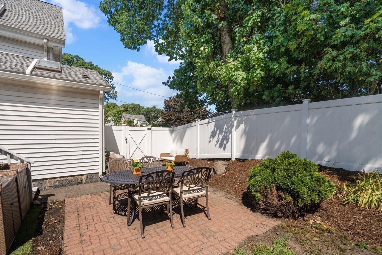Brick patio with outdoor dining set, lounge chairs, and white privacy fencing beside the house.