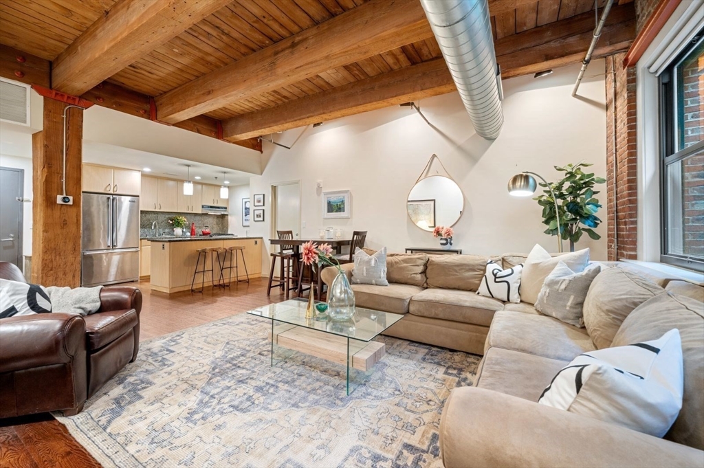 Open-plan loft living room with exposed timber beams, a beige sectional, and an adjoining kitchen.